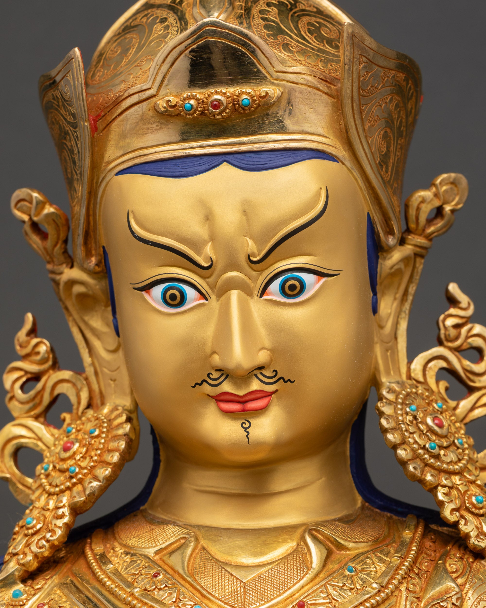 Detailed close-up of Guru Rinpoche Statue face with serene expression and gold-painted features