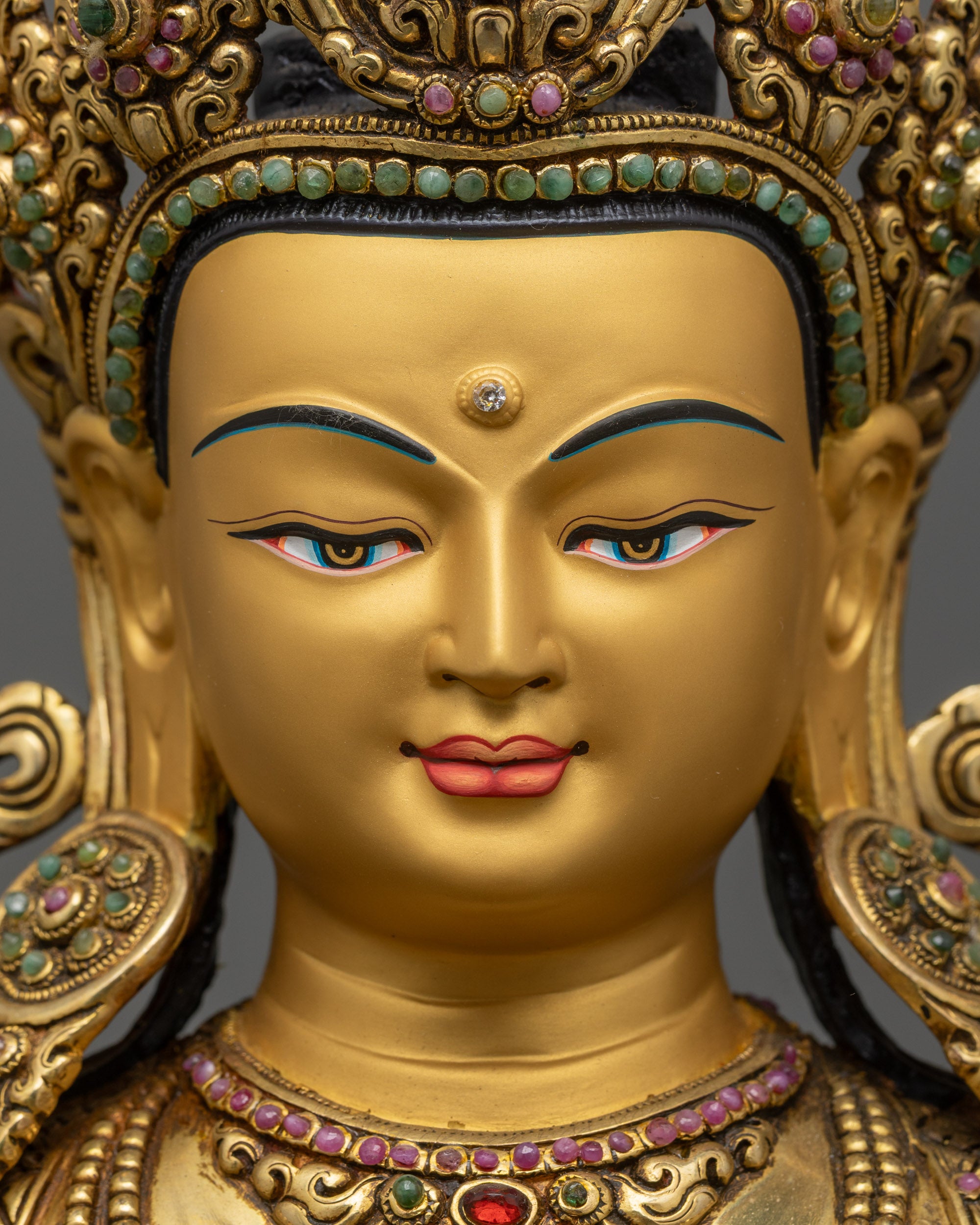 Detailed close up face of Chenrezig statue showing serene expression and gold detailing
