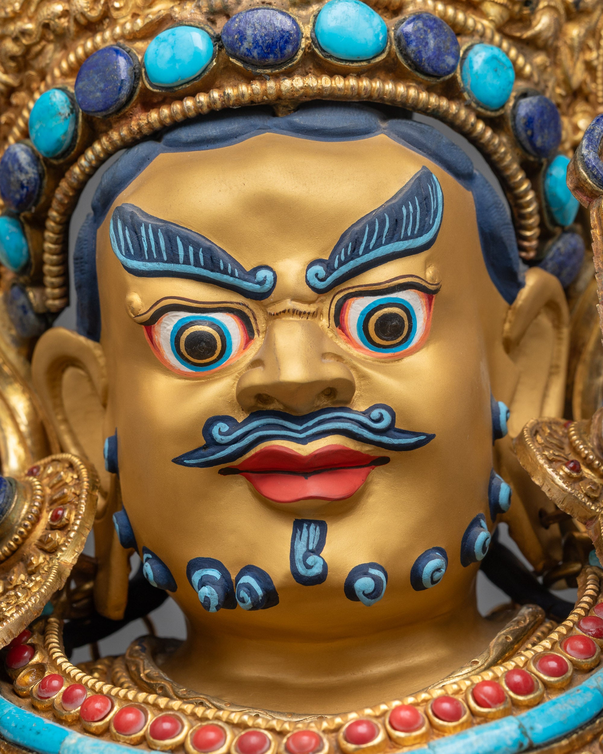 Detailed close up face of Crowned Dzambhala showing gold-gilded features and fierce expression
