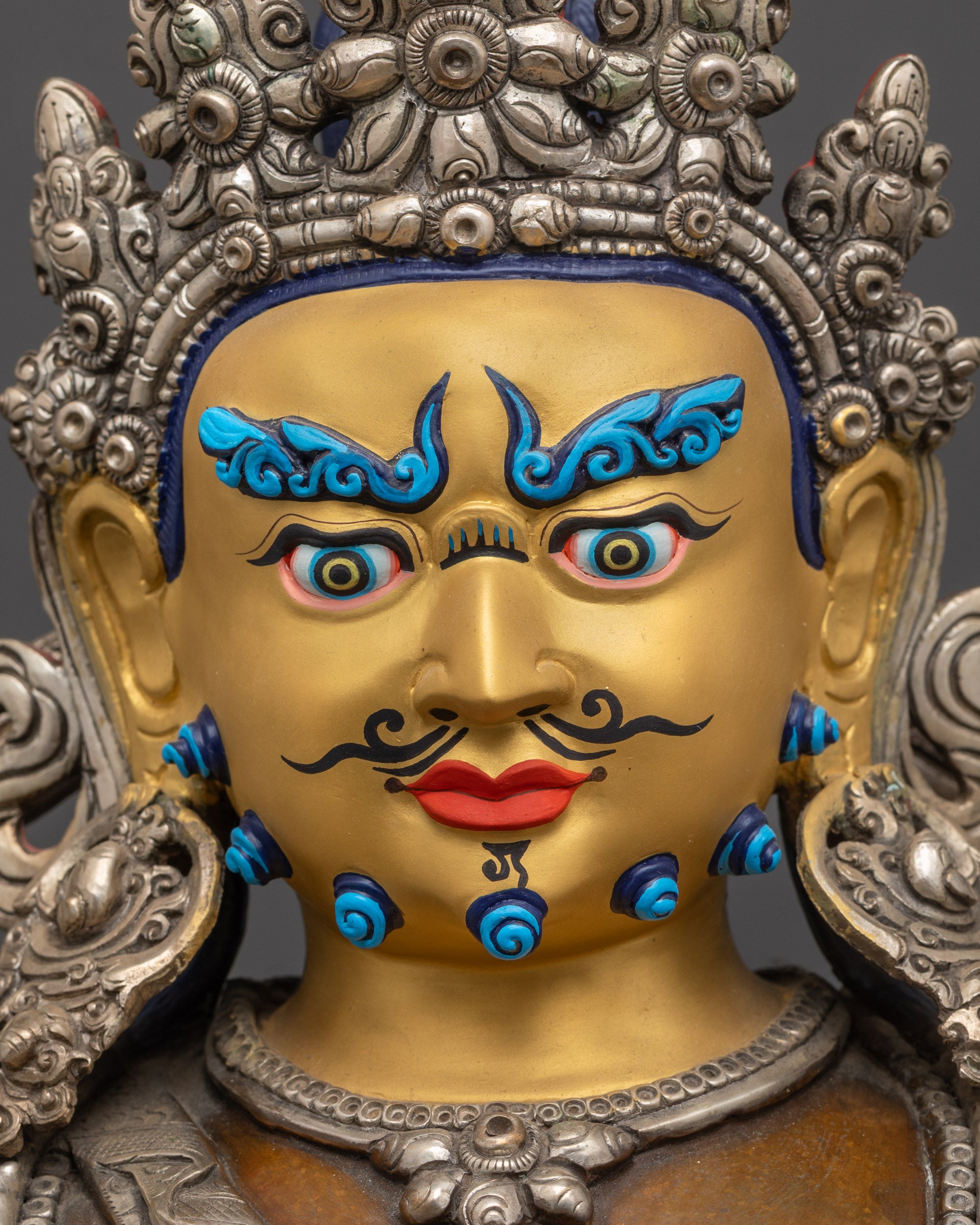 Detailed close up face of Dzambhala statue showing semi-wrathful gold-gilded facial expression
