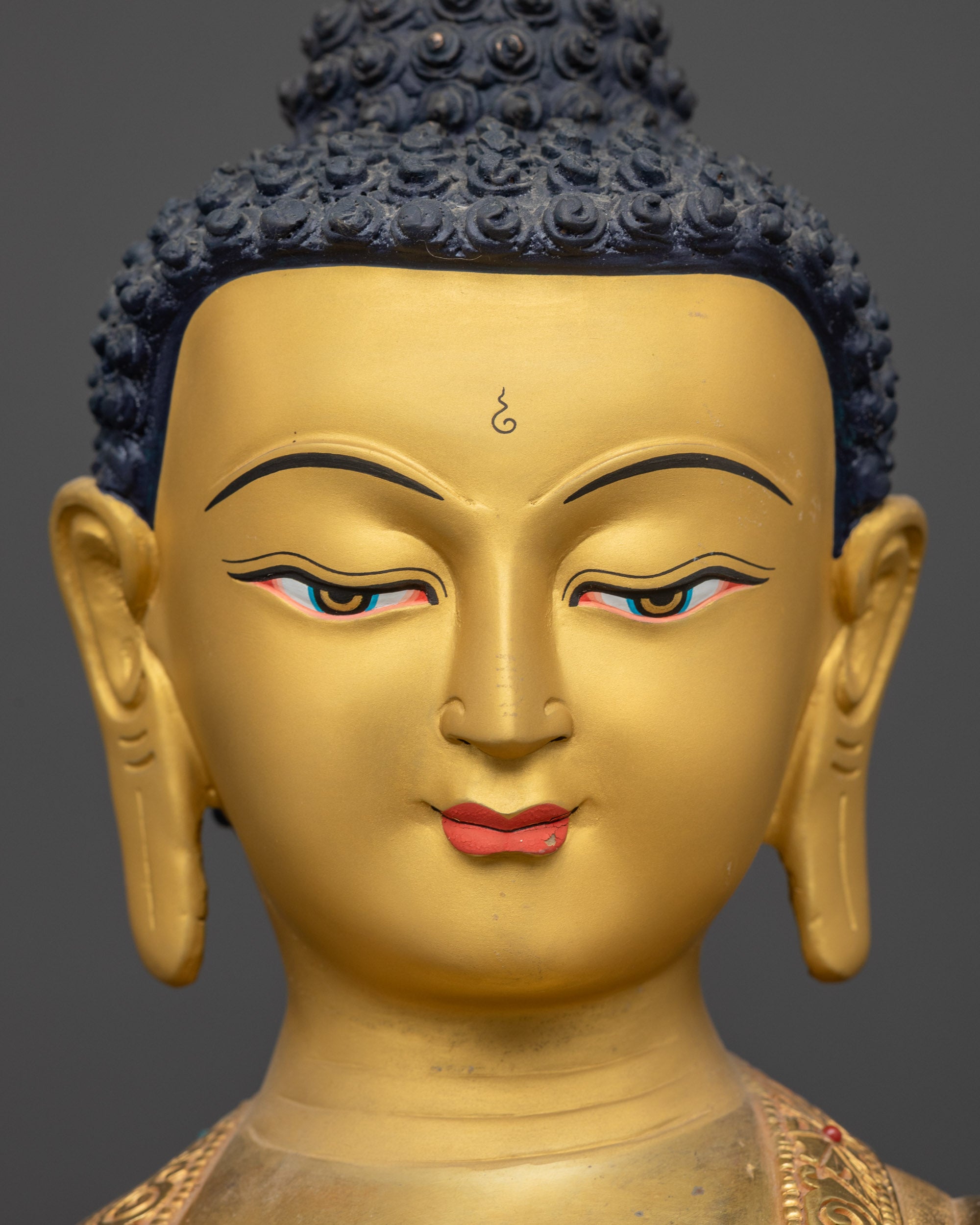 Detailed close up face of Medicine Buddha Bhaisajyaguru with serene gold-gilded expression
