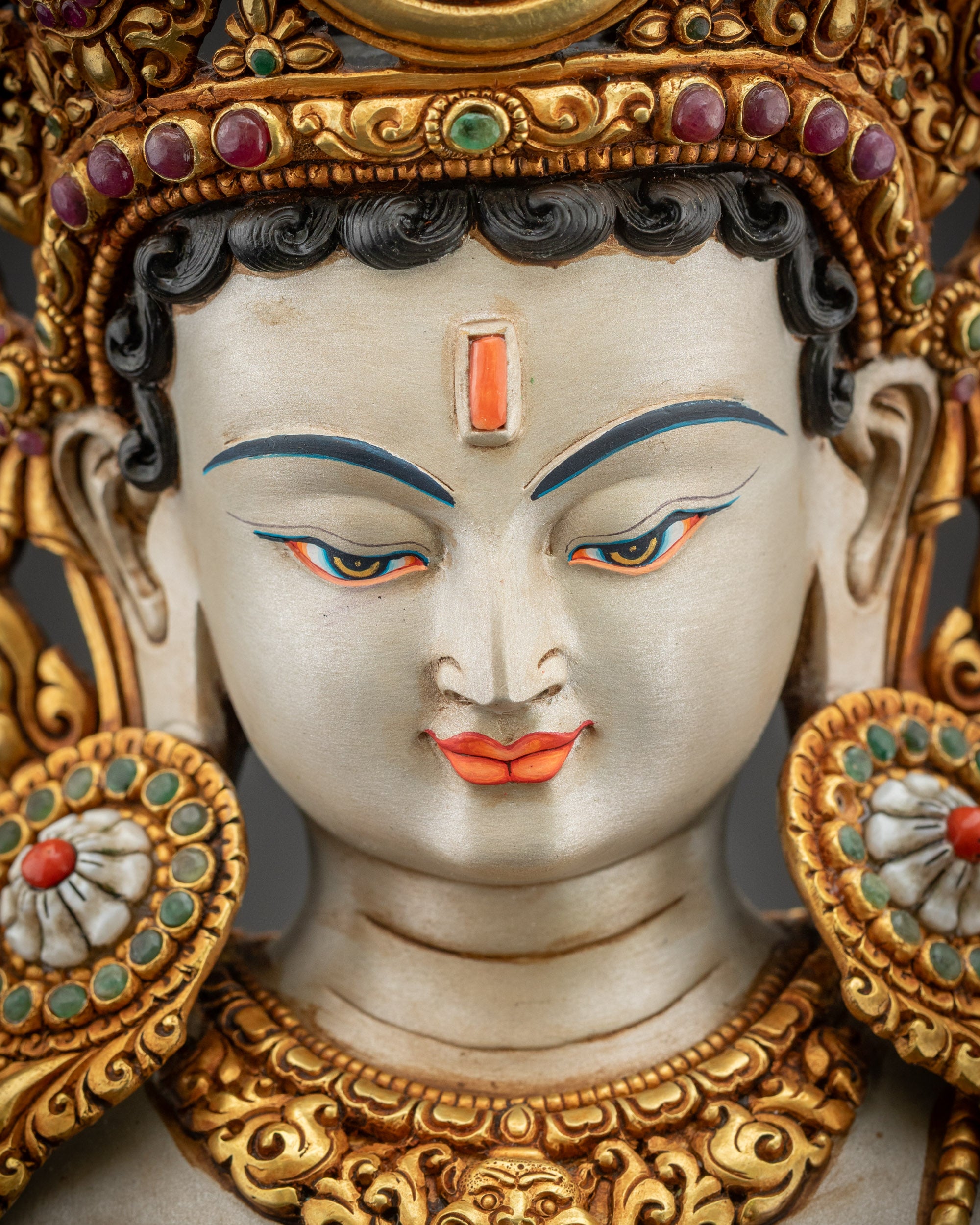 Detailed close up face of Padmapani Lokeshvara with serene expression and gold ornaments
