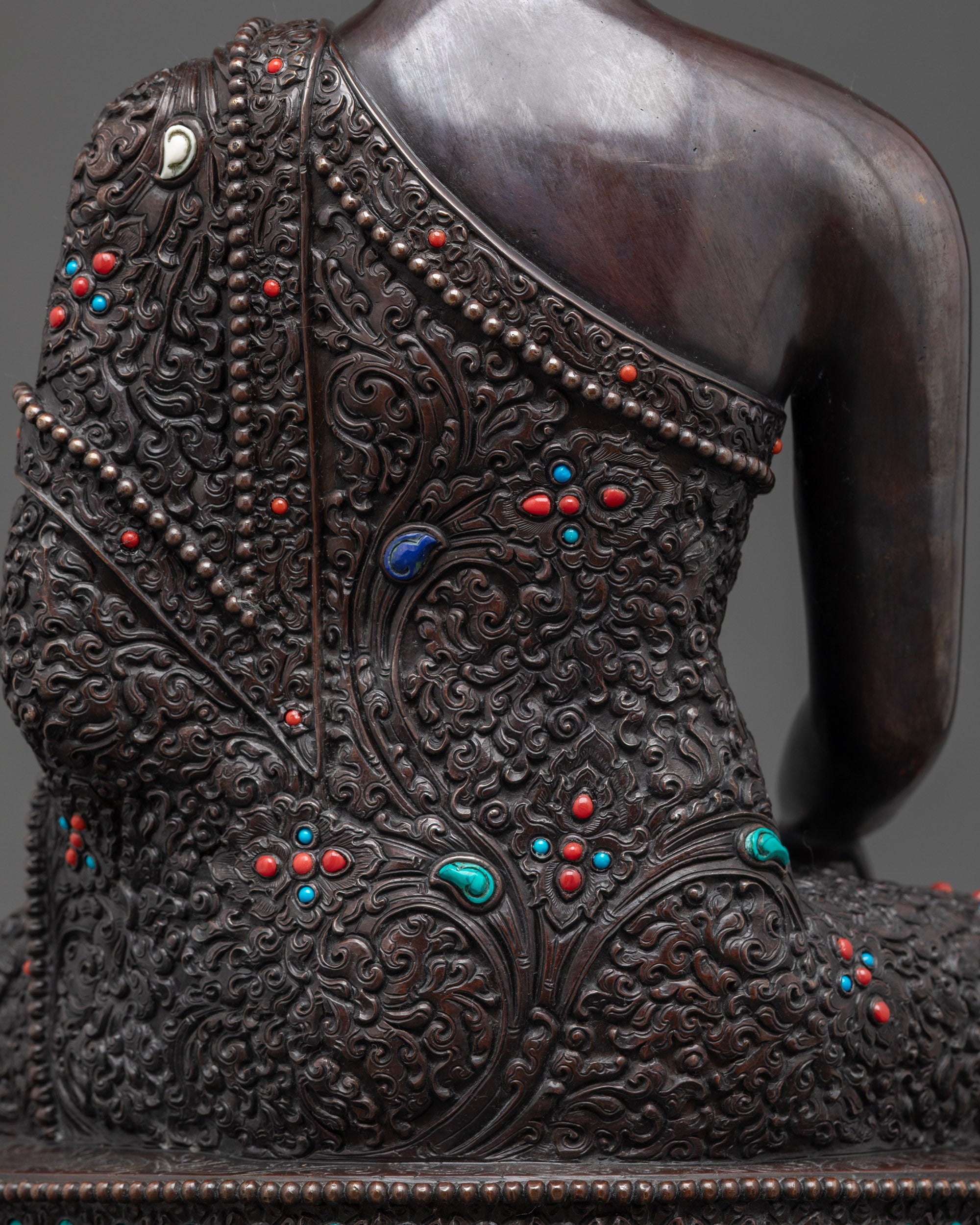 Detailed shot of monk's robe Buddha Shakyamuni oxidized statue with carvings & stones
