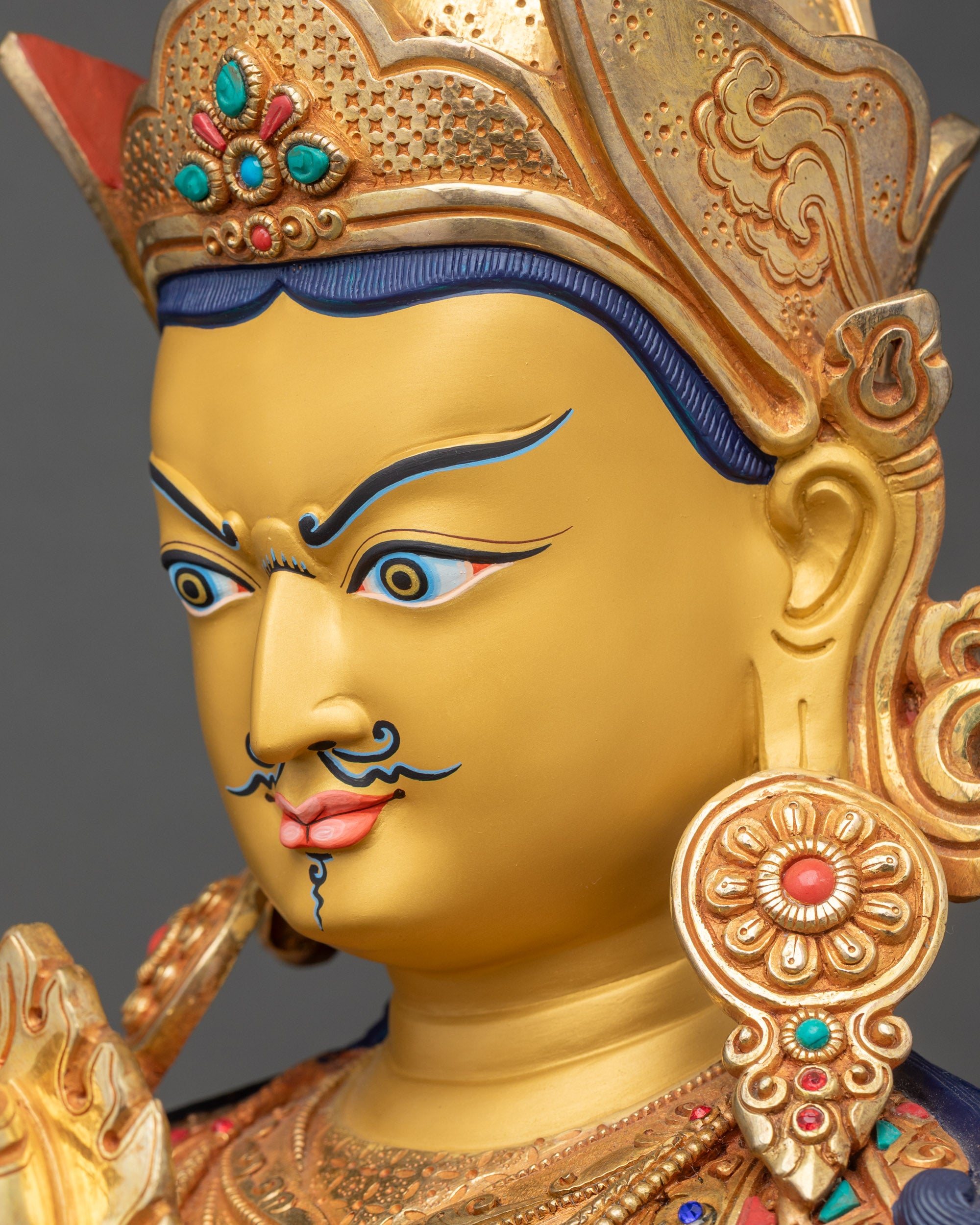 Detailed side close-up of Guru Norlha face capturing expressive gold-painted features and lotus hat with vulture feather