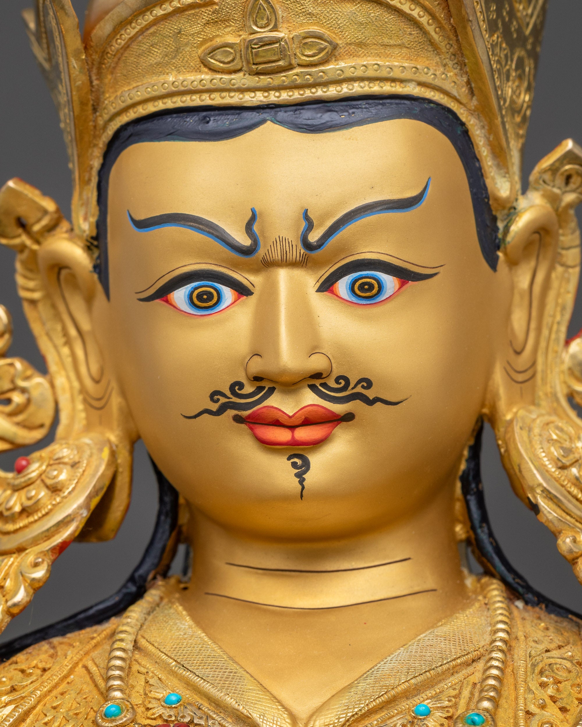 Detailed view of Guru Rinpoche statue gold-gilded face with semi-wrathful expression