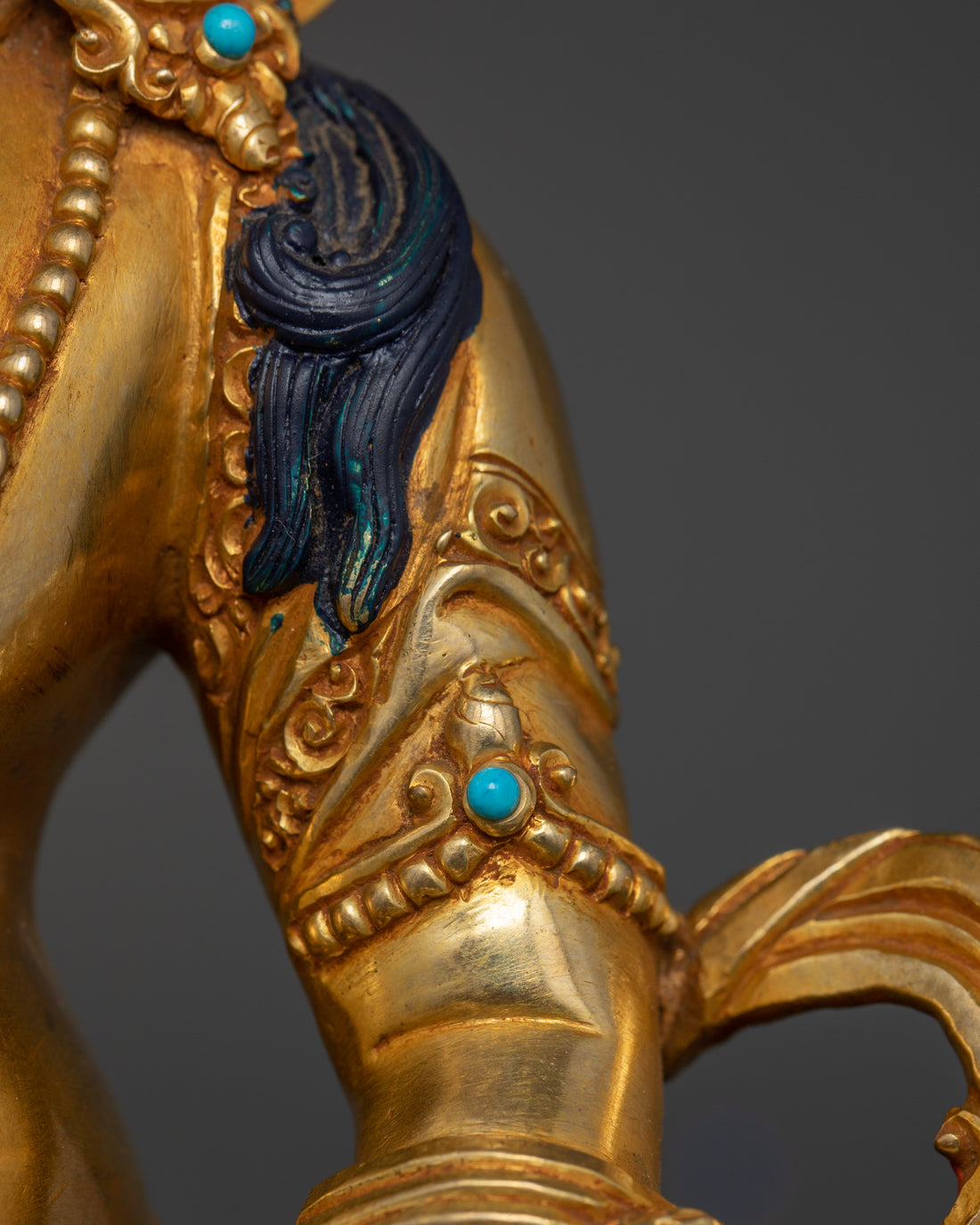 Close-up view of Dzambhala’s left arm featuring intricate details.