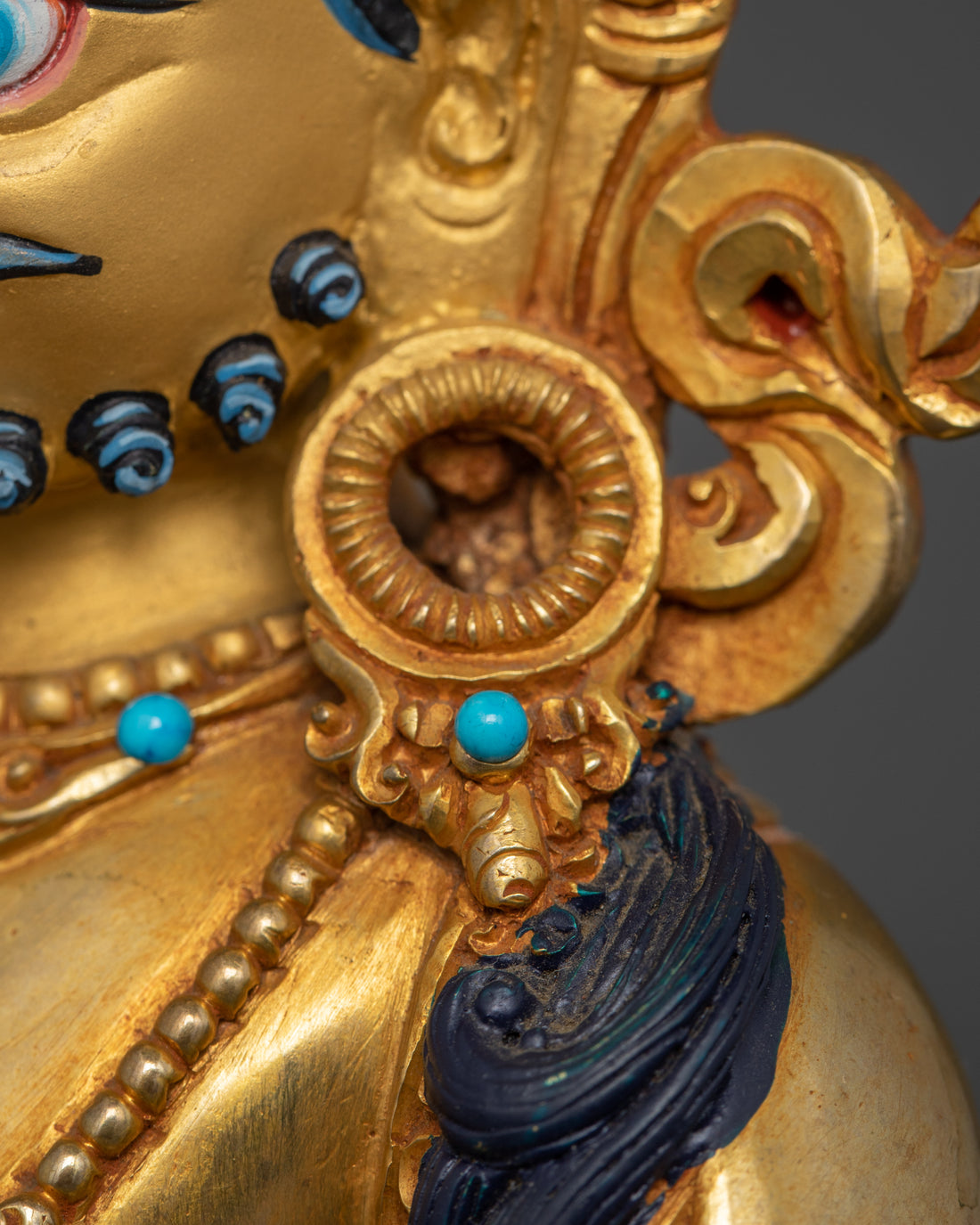 Close-up view of Dzambhala’s left ear adorned with a jewel, enhancing the deity’s regal appearance.