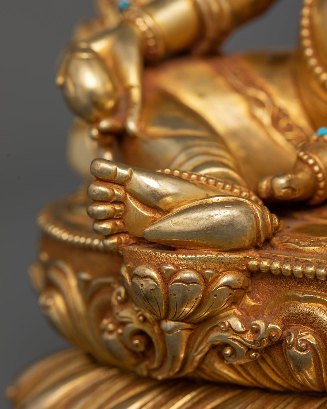 Close-up view of Dzambhala’s right leg, depicting it in a relaxed posture atop a lotus base.