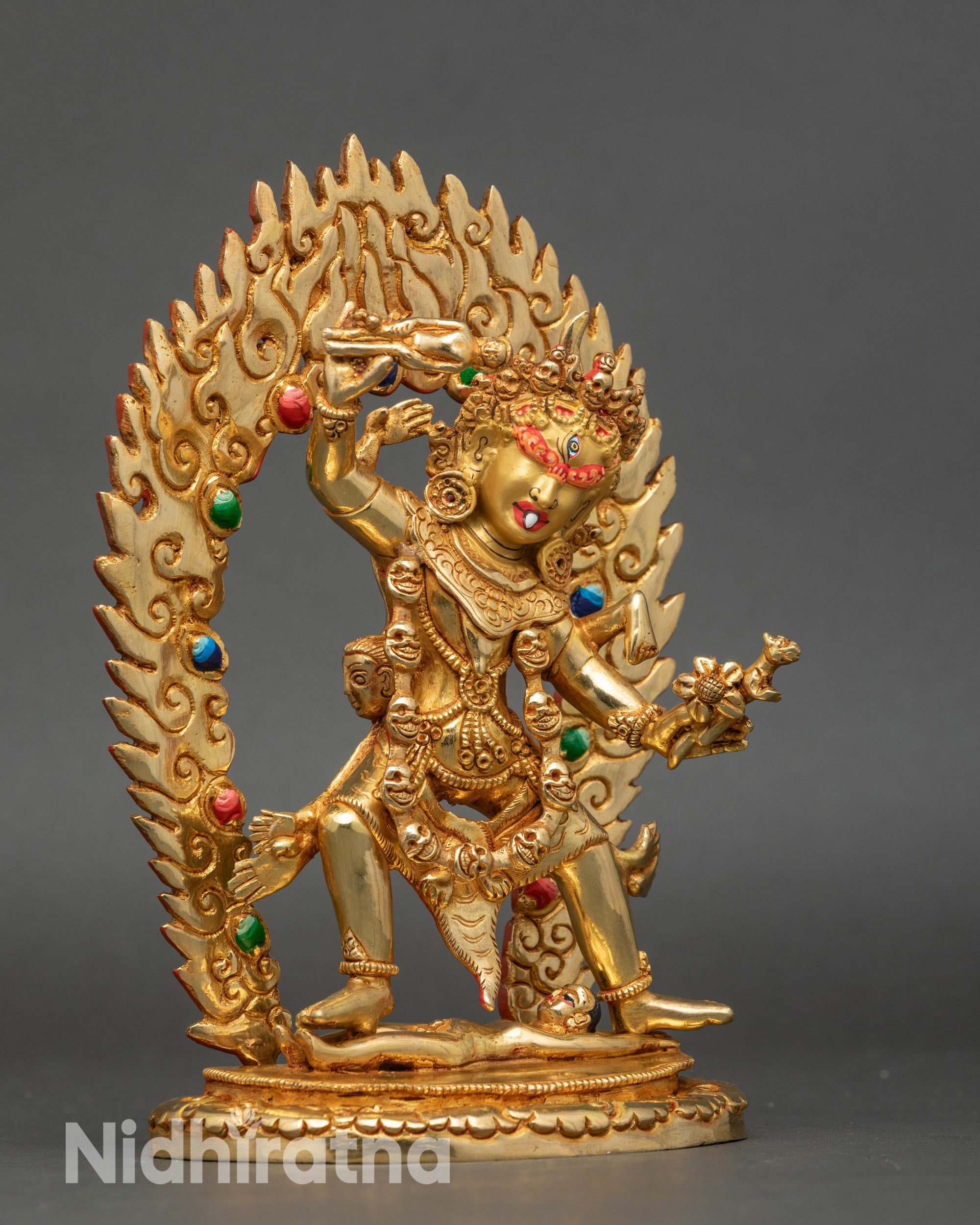 Side view: Side view Ekajati statue holding human, standing on another, gold-gilded, flame halo