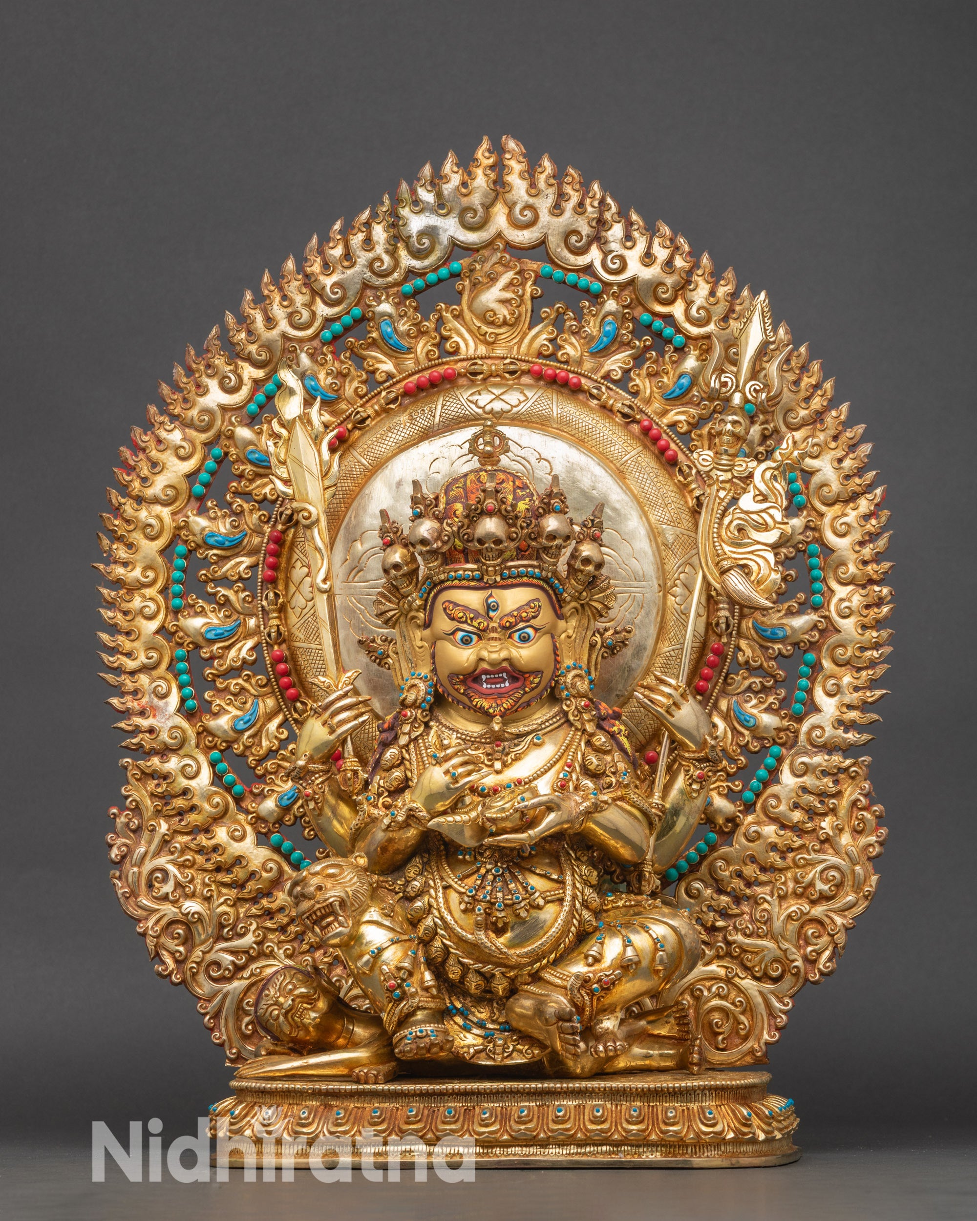 Front view Four-Armed Mahakala statue, 24k gold-gilded copper, seated on lotus with flame halo.