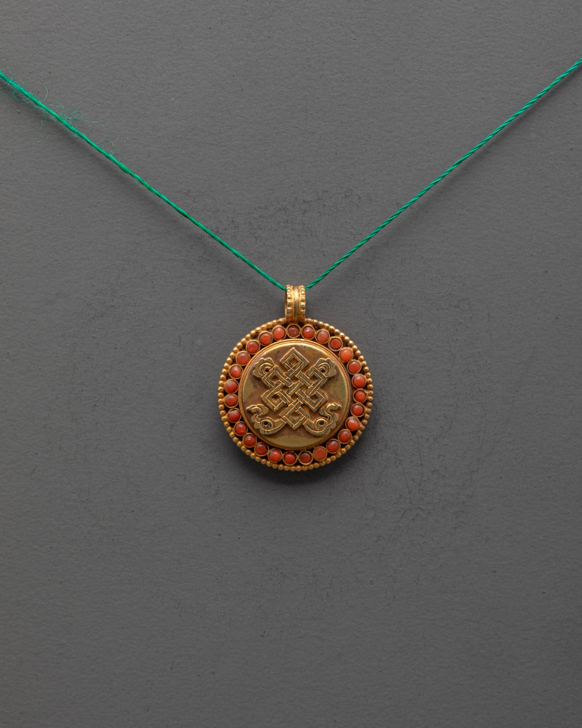 Front view of Endless Knot Locket with coral stones and gold-plated copper finish from Nepal