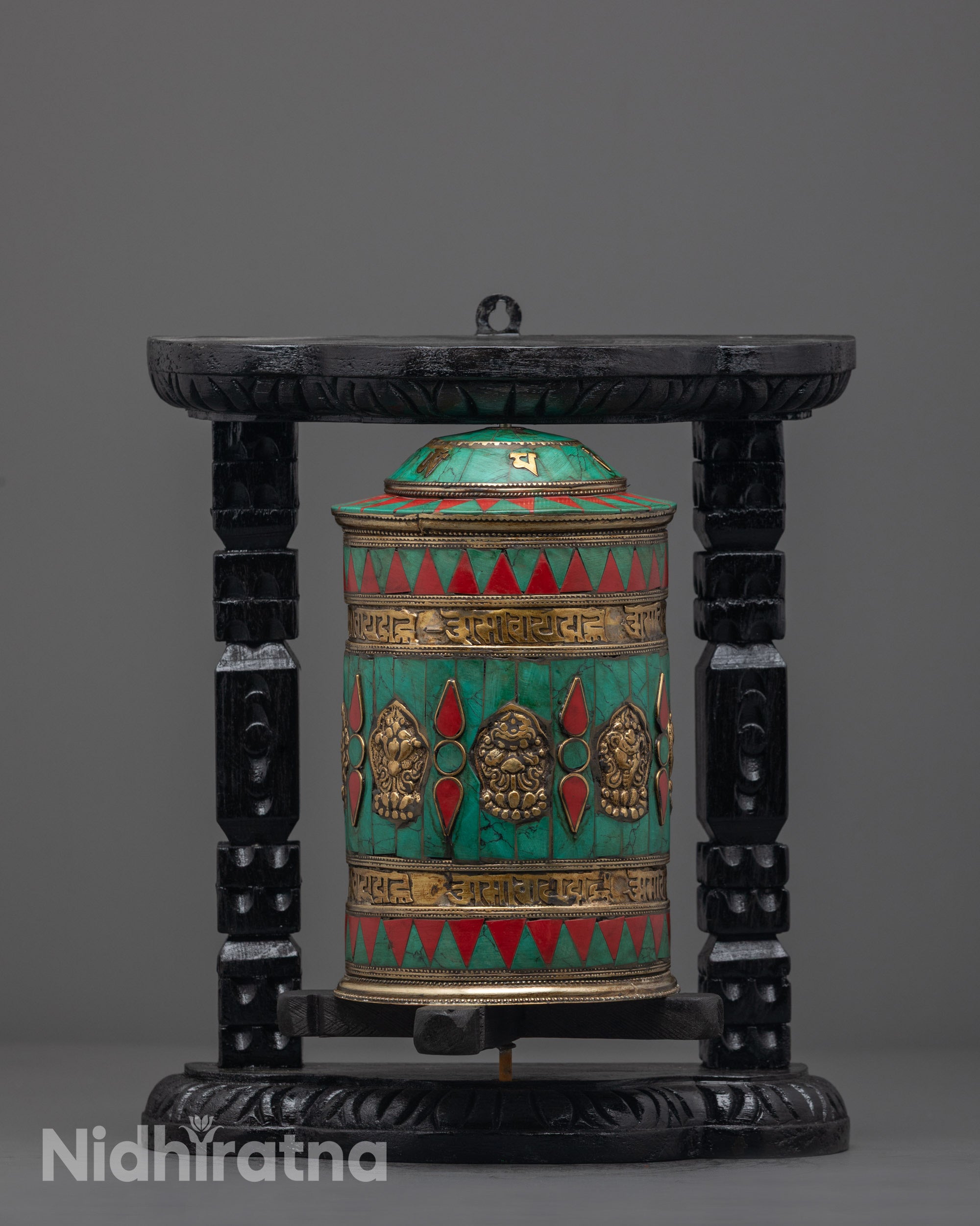 Front view of copper Auspicious Prayer Wheel with turquoise, coral, and engraved mantras on dark wood frame
