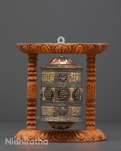 Front view of copper and brass Mantra Prayer Wheel with silver-plated symbols on wood frame