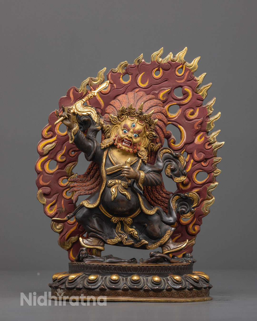 Front view of handcrafted Mahakala Statue with gold-gilded fierce face and crown crushing two humans
