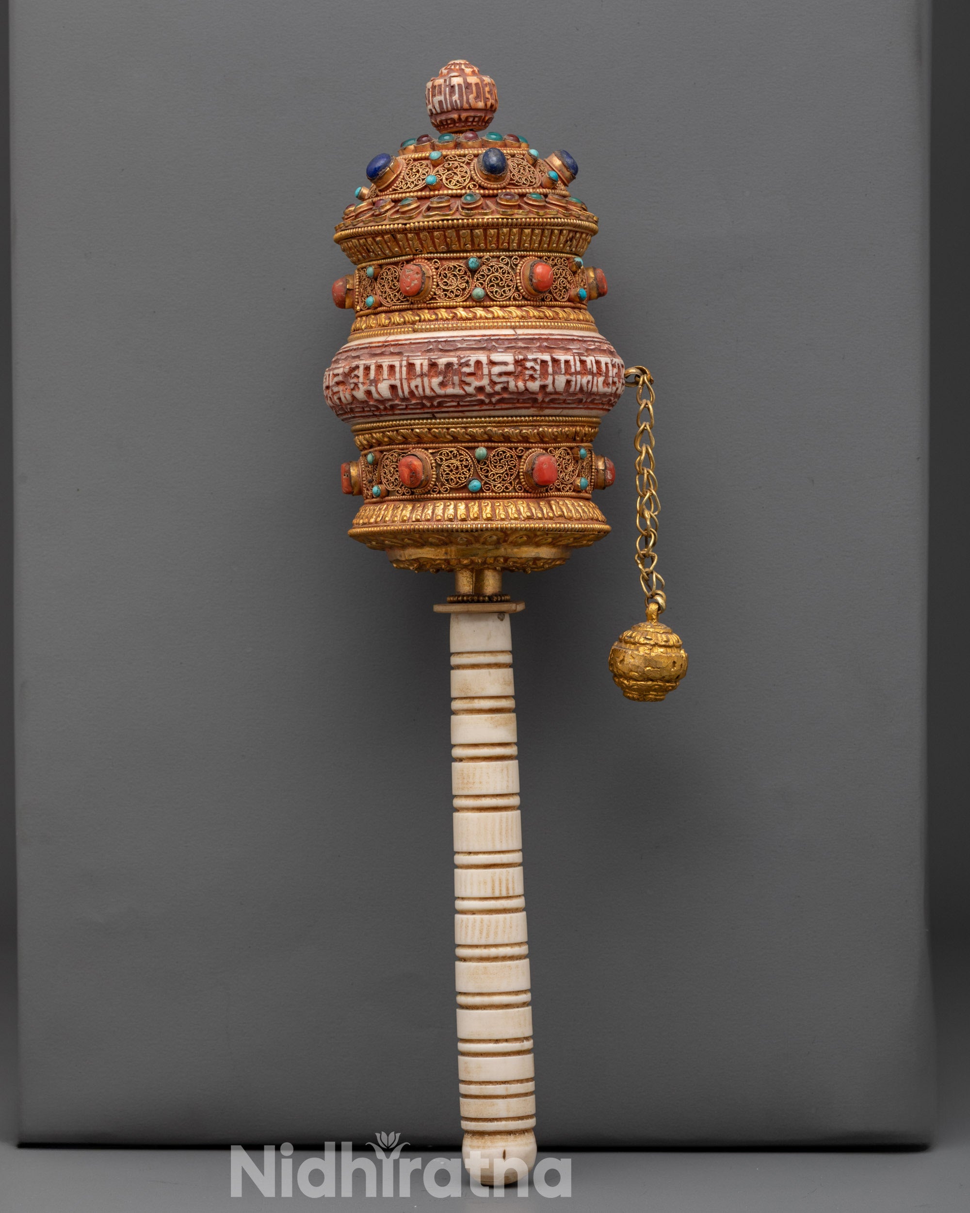 Front view of handheld copper mantra prayer wheel with gold-plated filigree and semi-precious stones