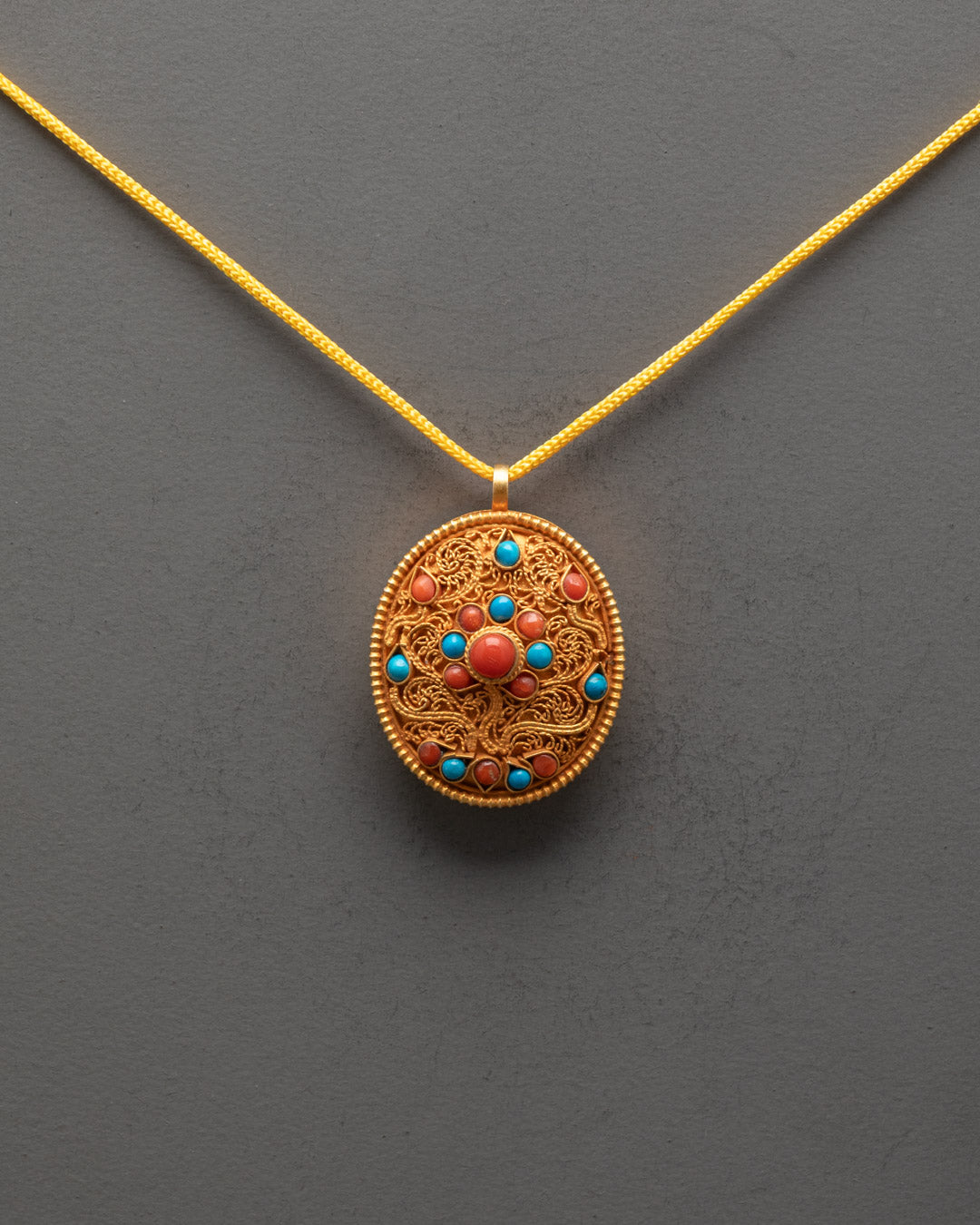Front view of oval Sacred Tibetan Locket Pendant with gold filigree and turquoise, coral stones
