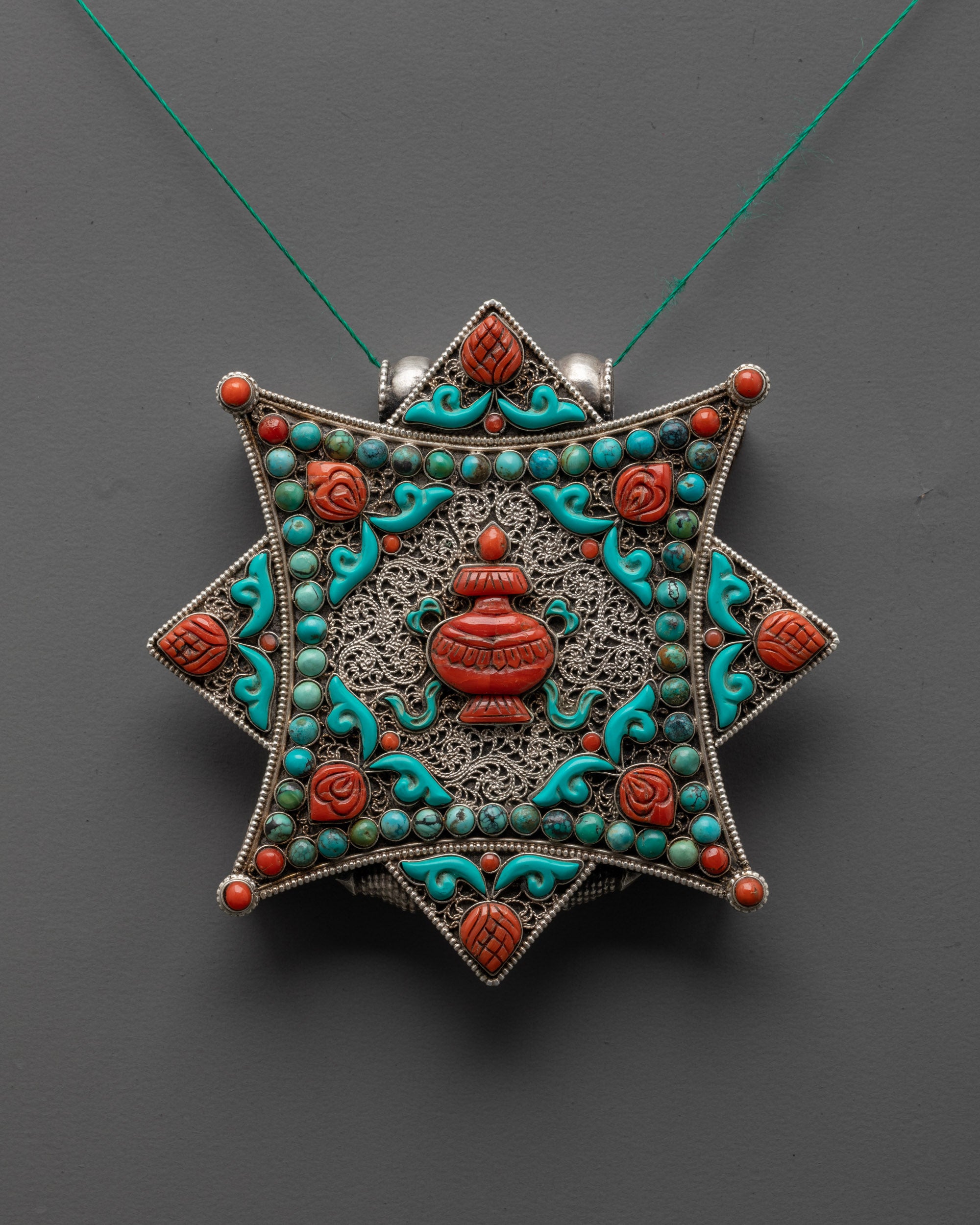 Front view of silver Kalash locket with turquoise vase and coral stone accents