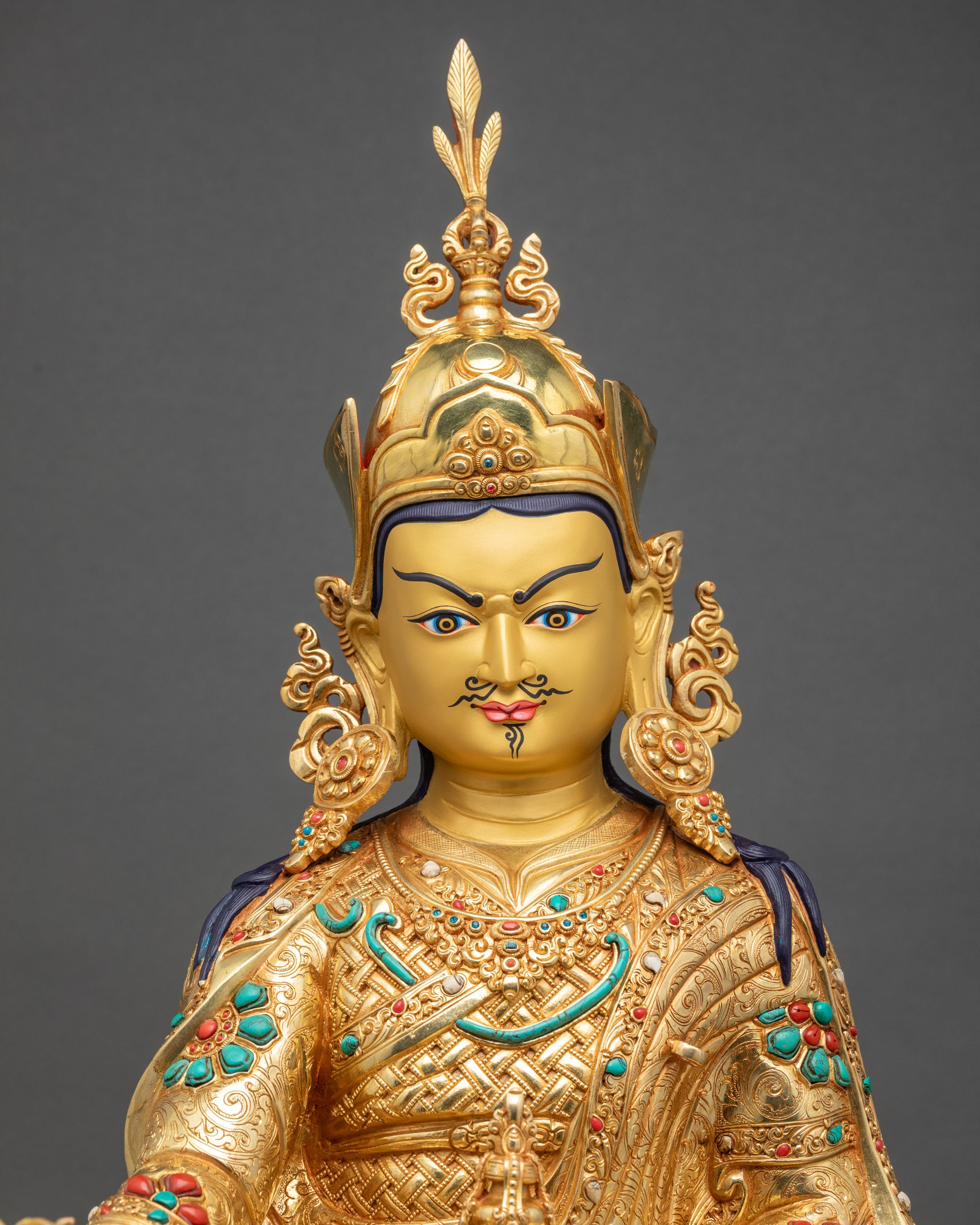 Close-up of Guru Rinpoche gold-painted face with serene expression Tibetan Buddhist statue