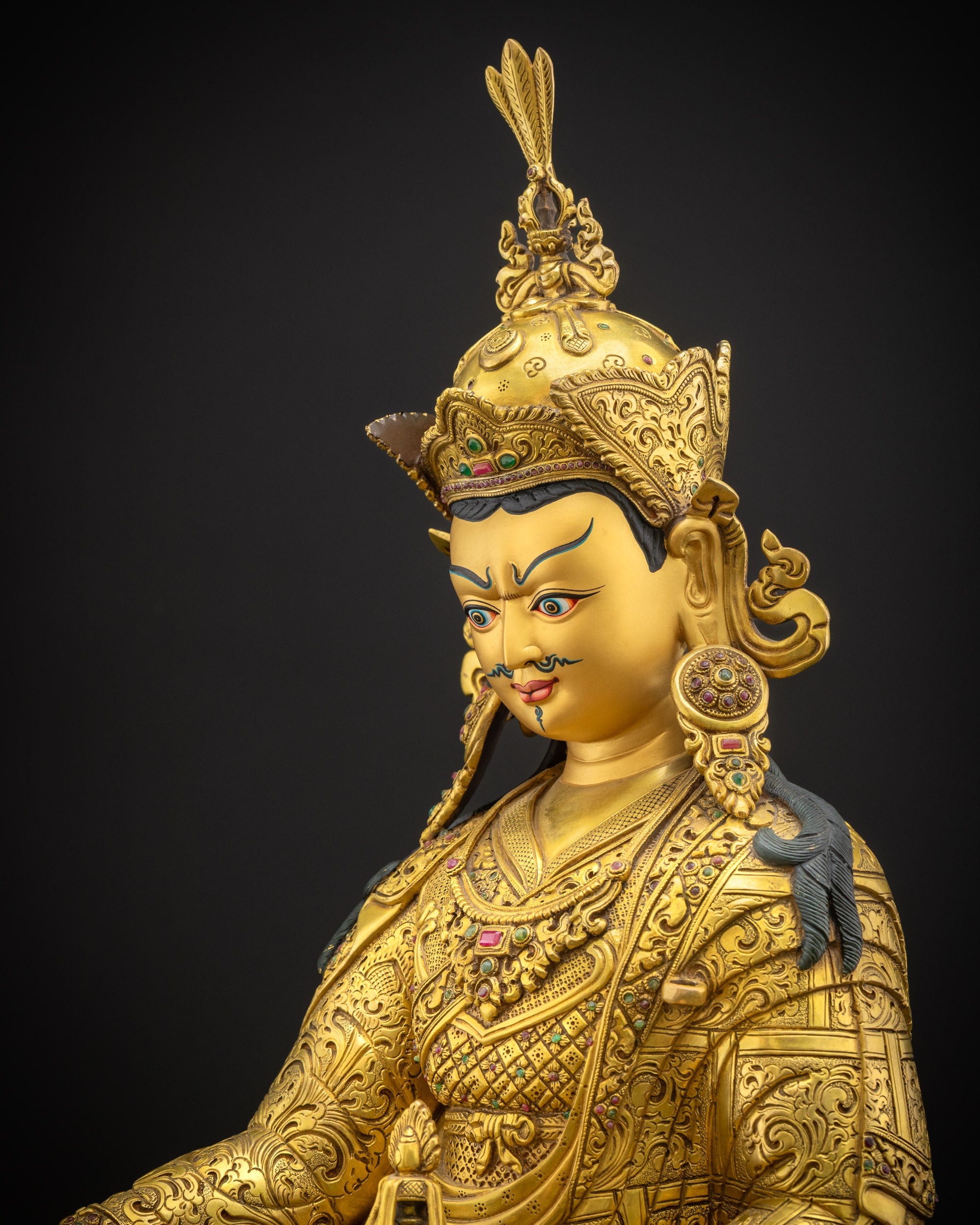 Side view close-up of Guru Rinpoche sculpture highlighting intricate kasaya robes and finely carved motif patterns