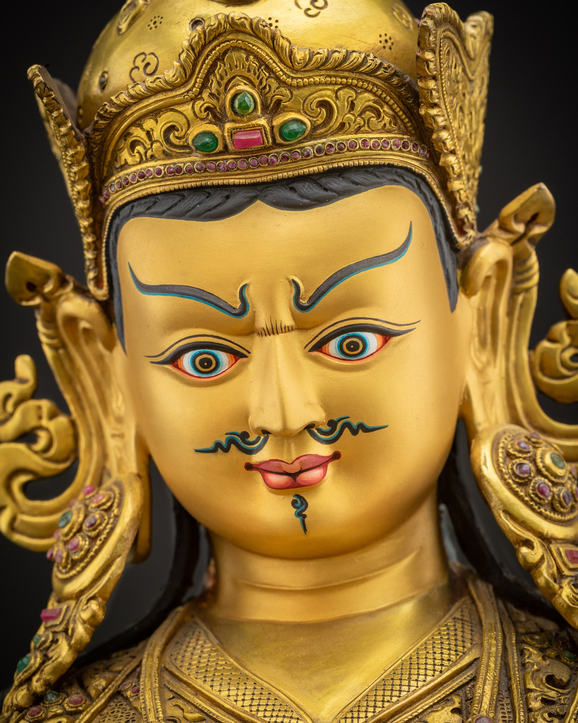 Detailed close-up of Guru Rinpoche sculpture’s radiant gold-gilded face, expressing compassion and spiritual wisdom