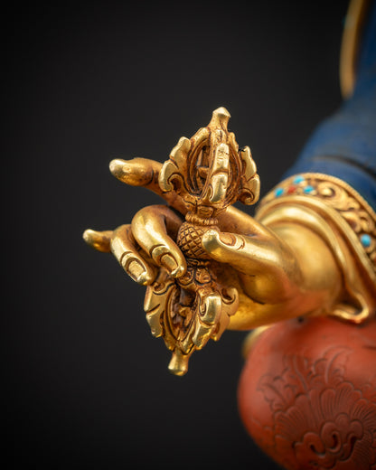 Close-up of Guru Rinpoche holding vajra, showing intricate copper carving and gold highlights.