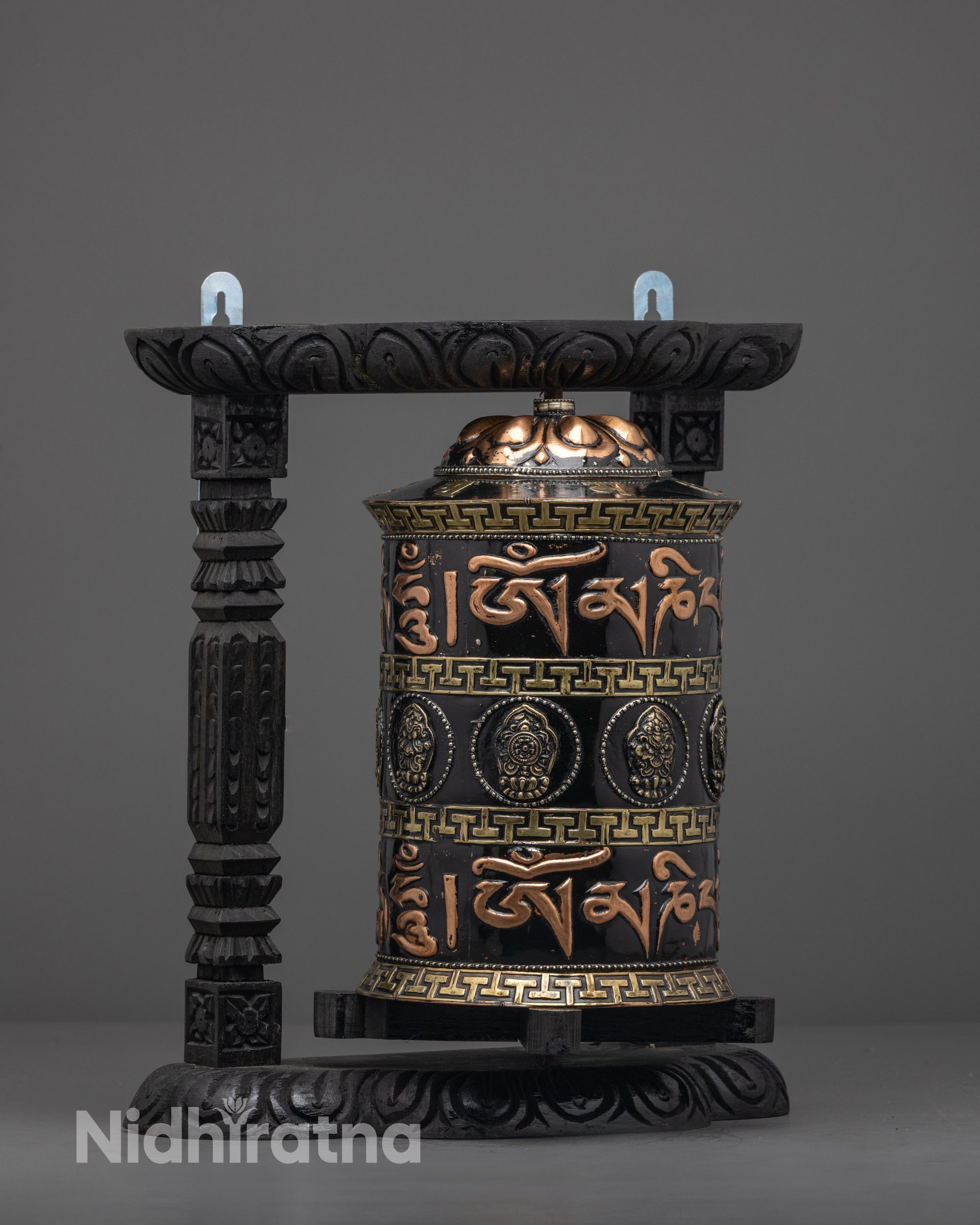 Intricately carved dark wood frame holding copper prayer wheel painted with black acrylic