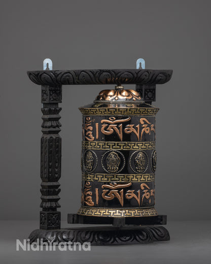 Intricately carved dark wood frame holding copper prayer wheel painted with black acrylic
