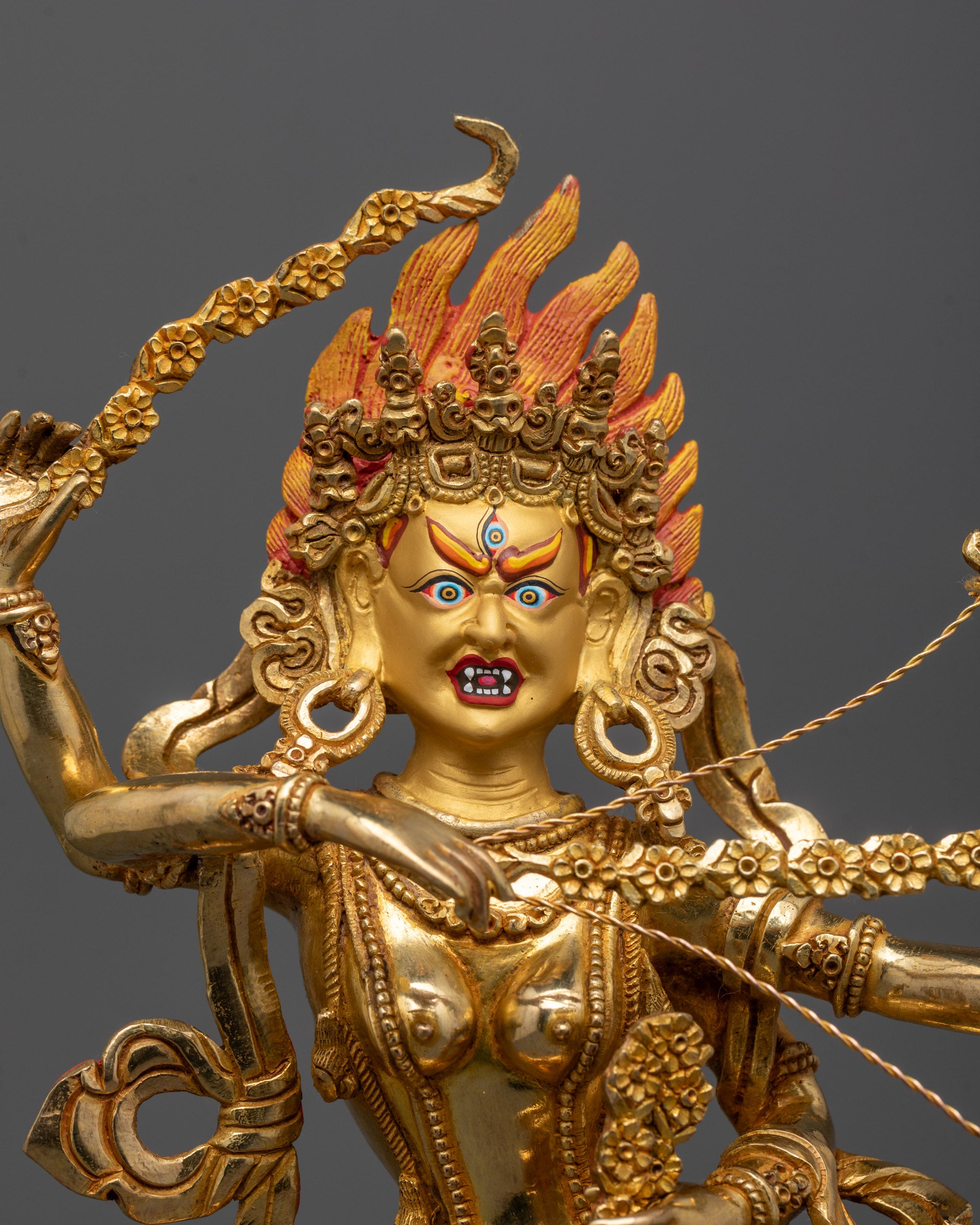 Close up of Kurukulla’s radiant gold fire-gilded body holding bow arrow and sword details