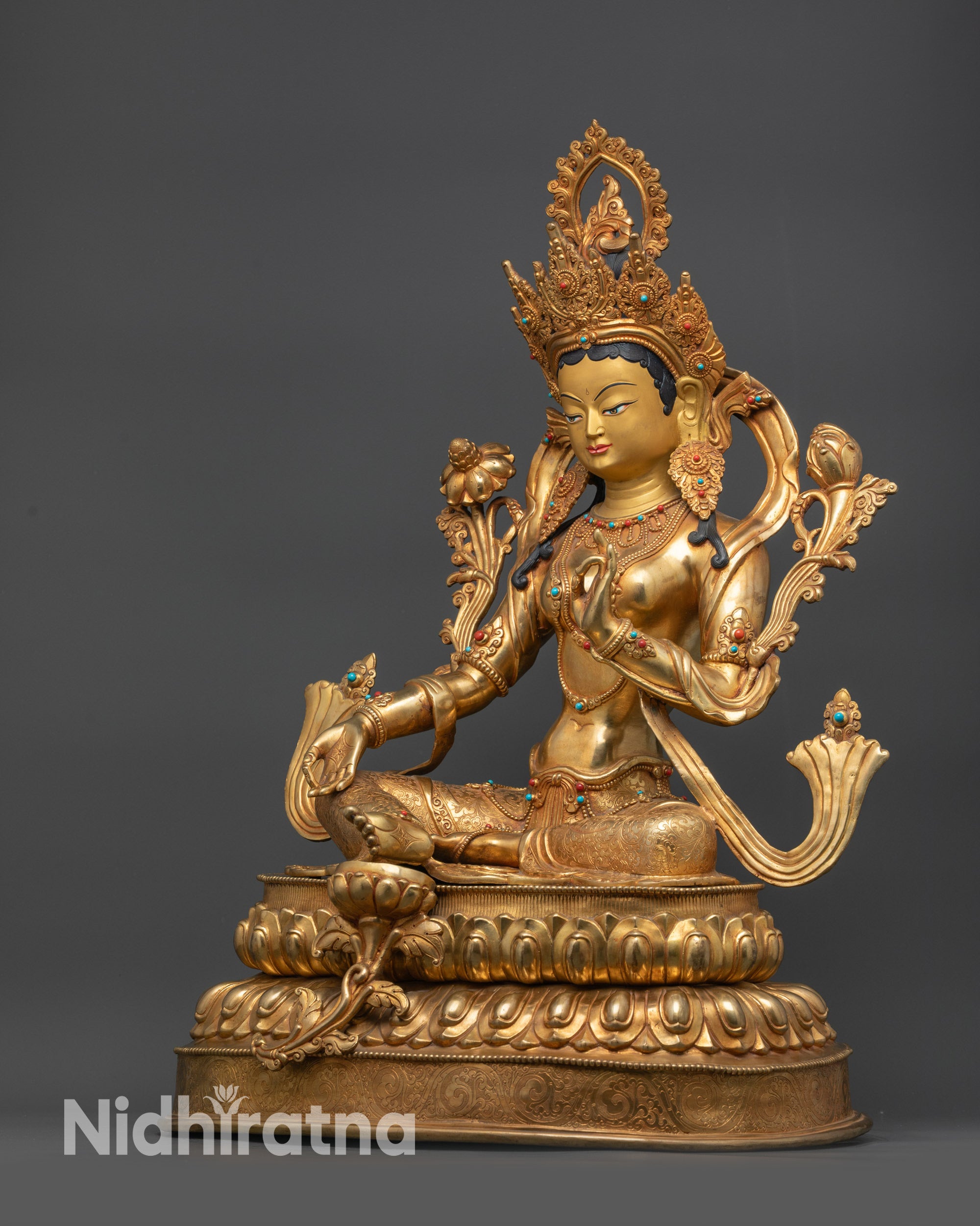 Left view side Green Tara statue holding utpala stem with lotus blossoms beside shoulder
