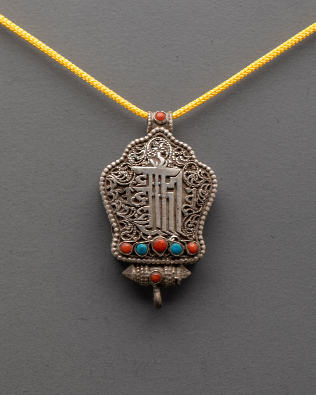 Close-up of intricate silver filigree and Kalachakra mantra engraving on Tibetan Ghau locket
