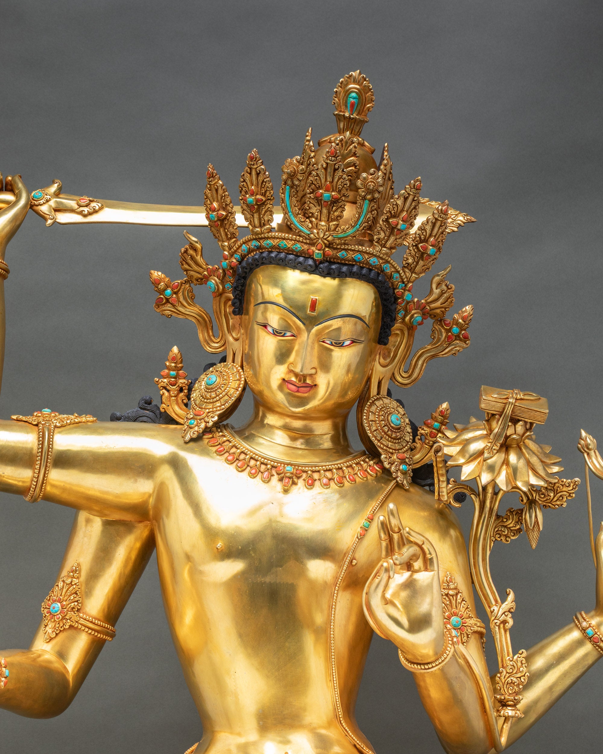 Maha Manjushri statue close-up showing four-armed Bodhisattva with flaming sword, utpala flower, and gold jewelry details