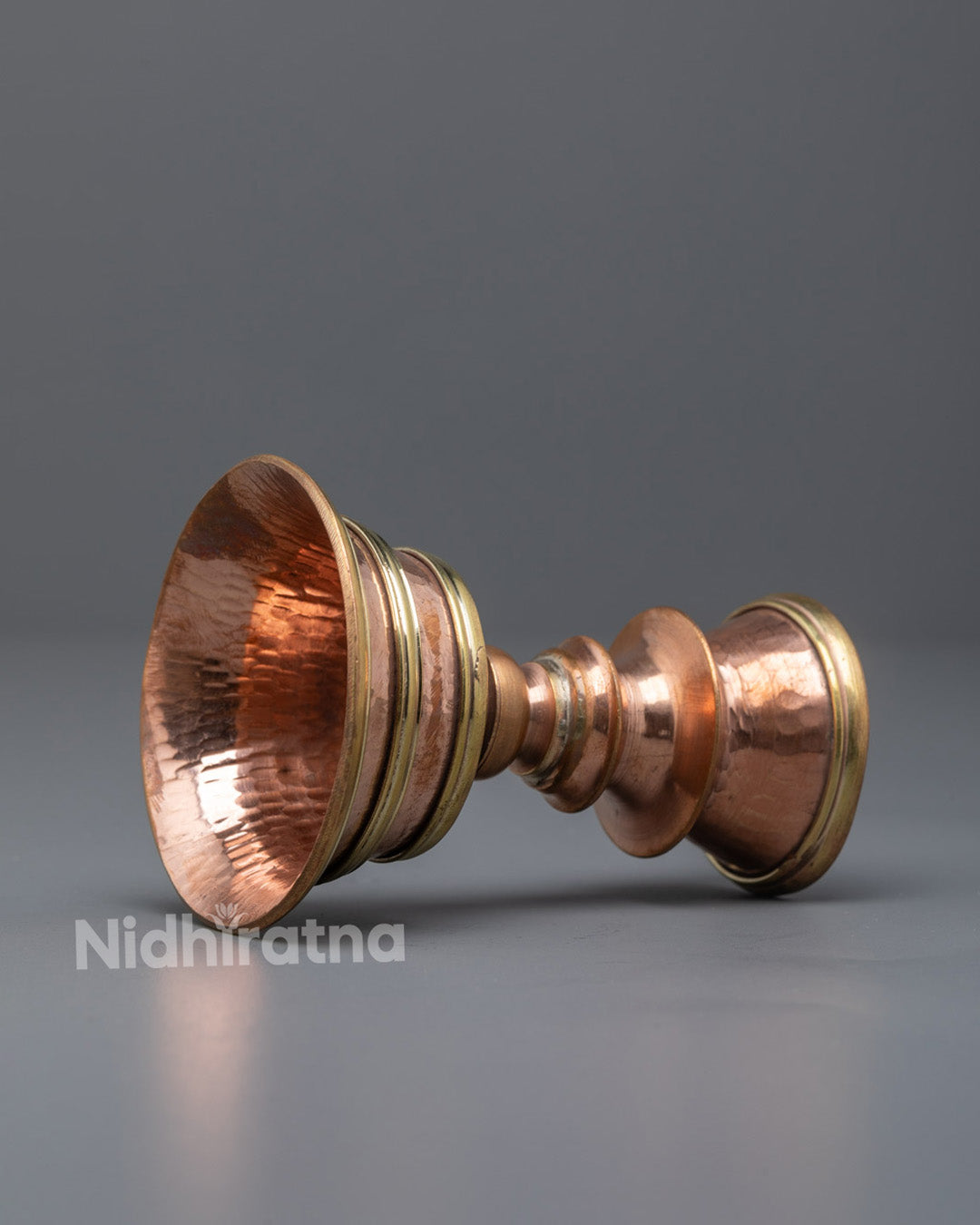 Side-view Nepalese artisan hand-shaping a traditional copper butter lamp using ancient metalwork