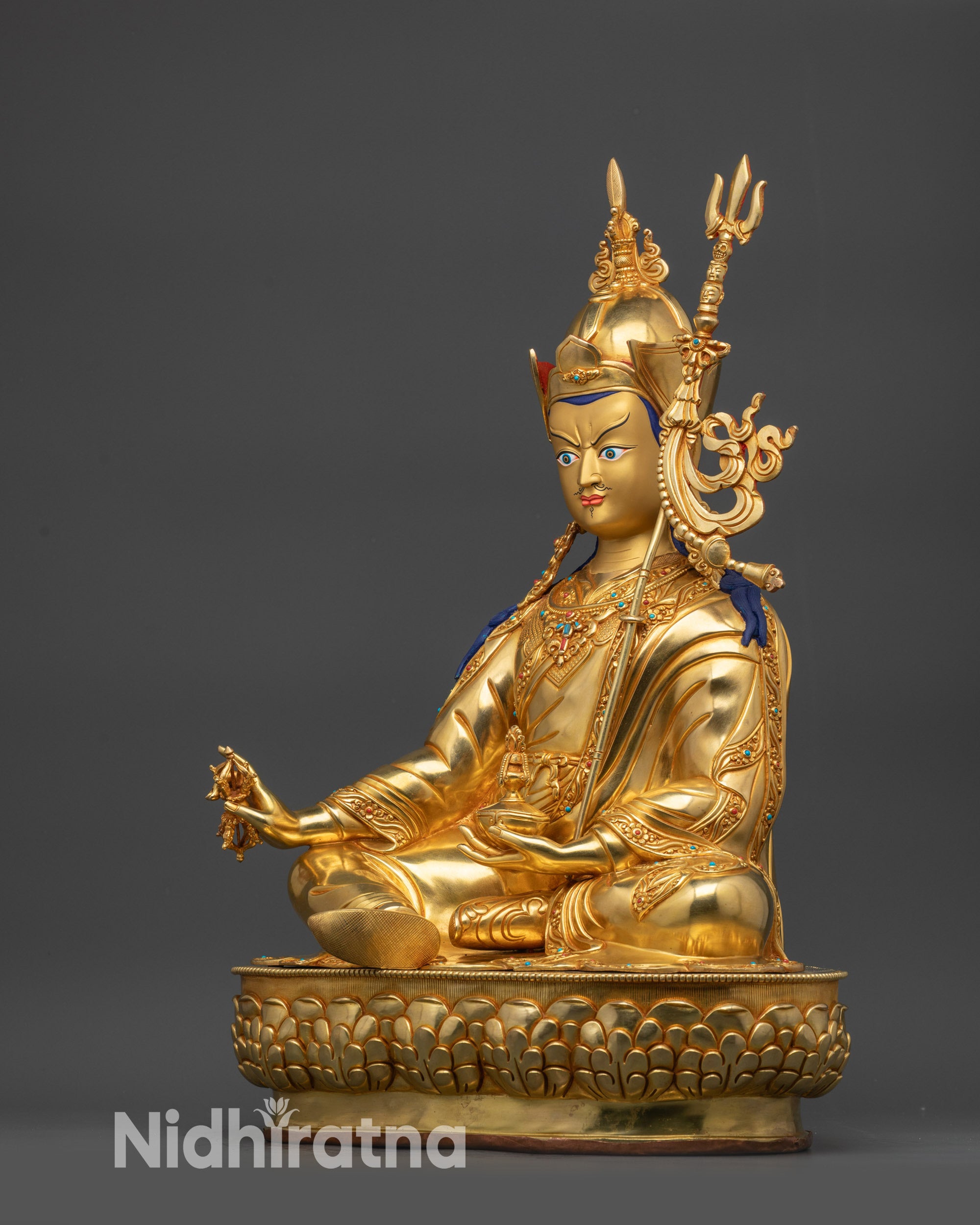 Right view side of Guru Rinpoche statue with trident resting on shoulder
