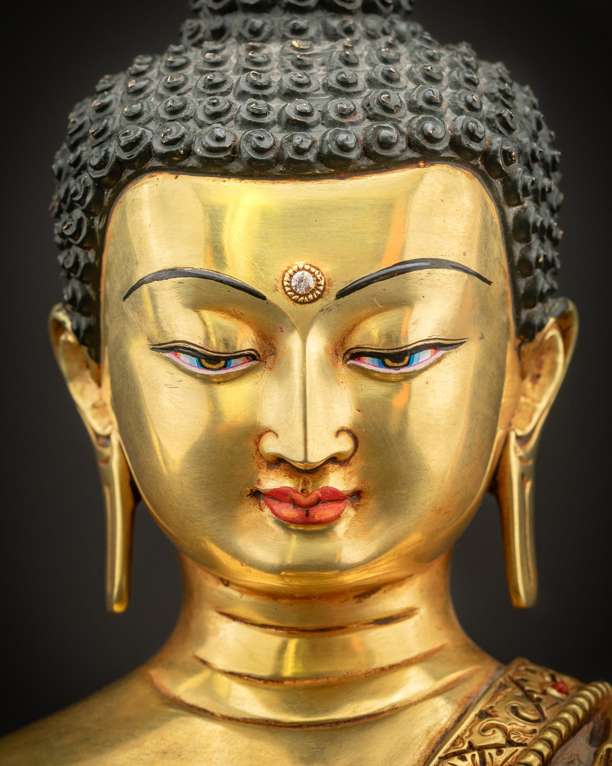 Detailed close-up of Shakyamuni Buddha face with calm expression, elongated earlobes, and gold gilded Nepalese craftsmanship.
