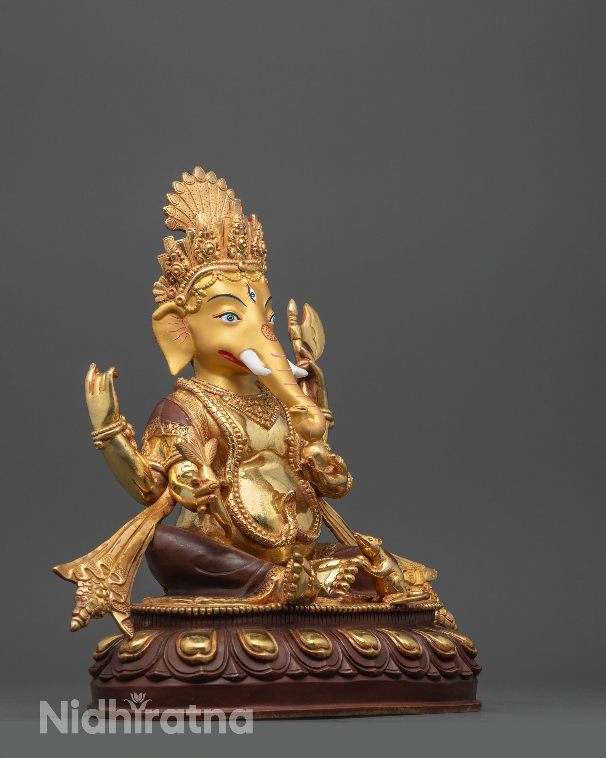Side angle of Ganesh statue showing flowing robe and four arms holding sacred objects