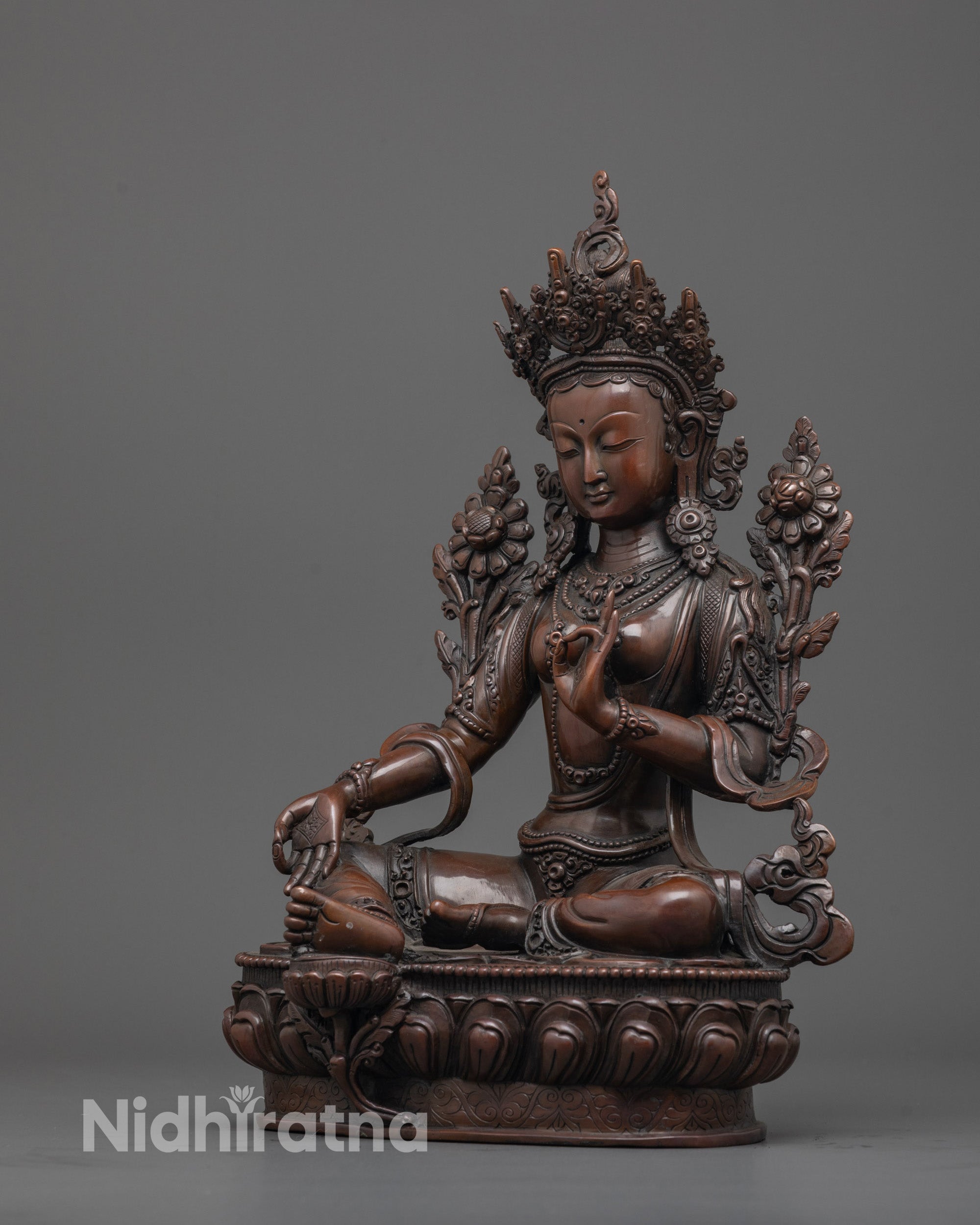 Side angle of Green Tara statue with carved jewelry and delicate utpala flower in royal pose.