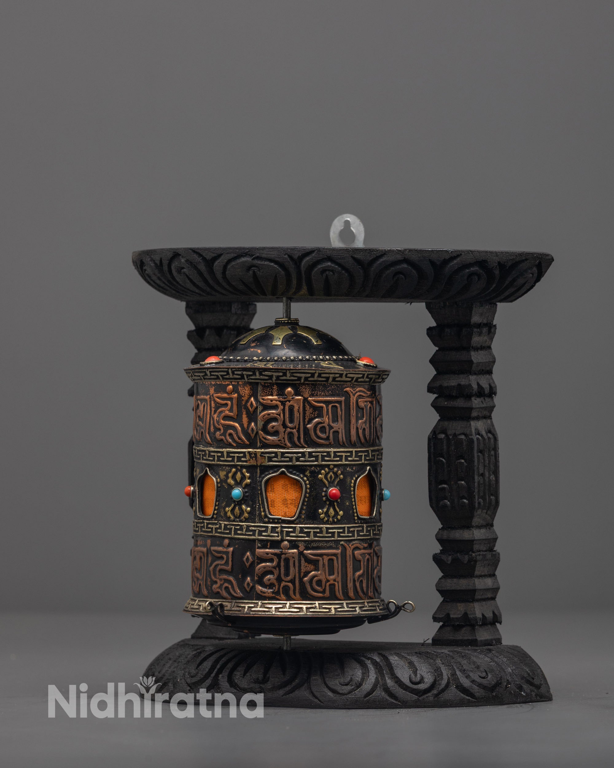 Side angle of Tibetan mantra prayer wheel on carved dark wood frame