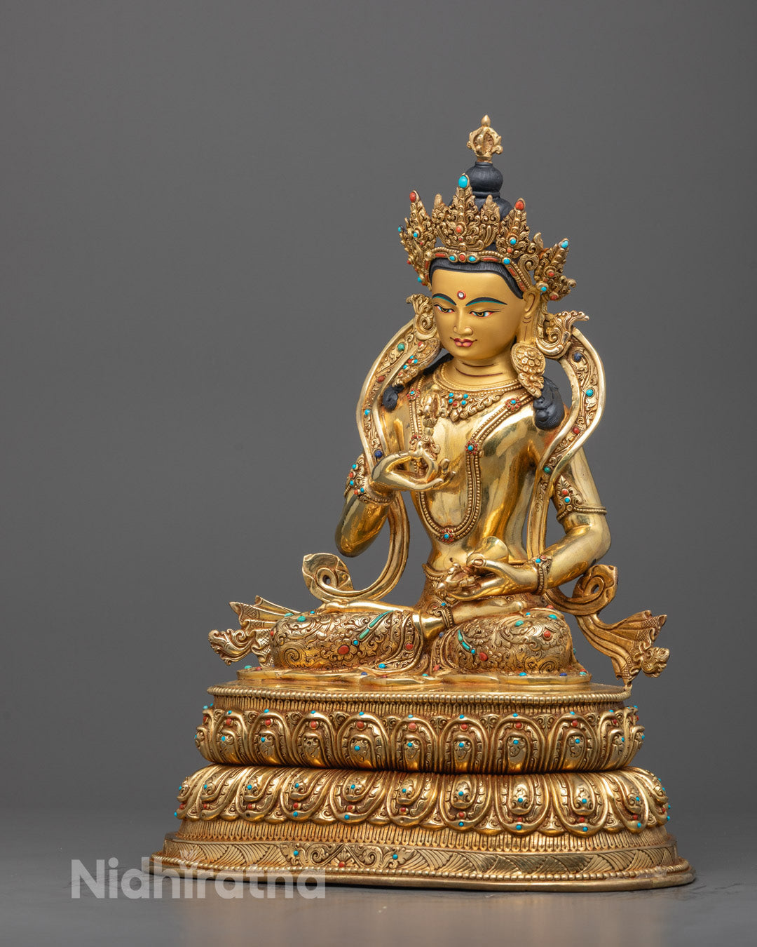Side angle of gold fire-gilded Vajrasattva statue holding vajra and bell, lotus base visible