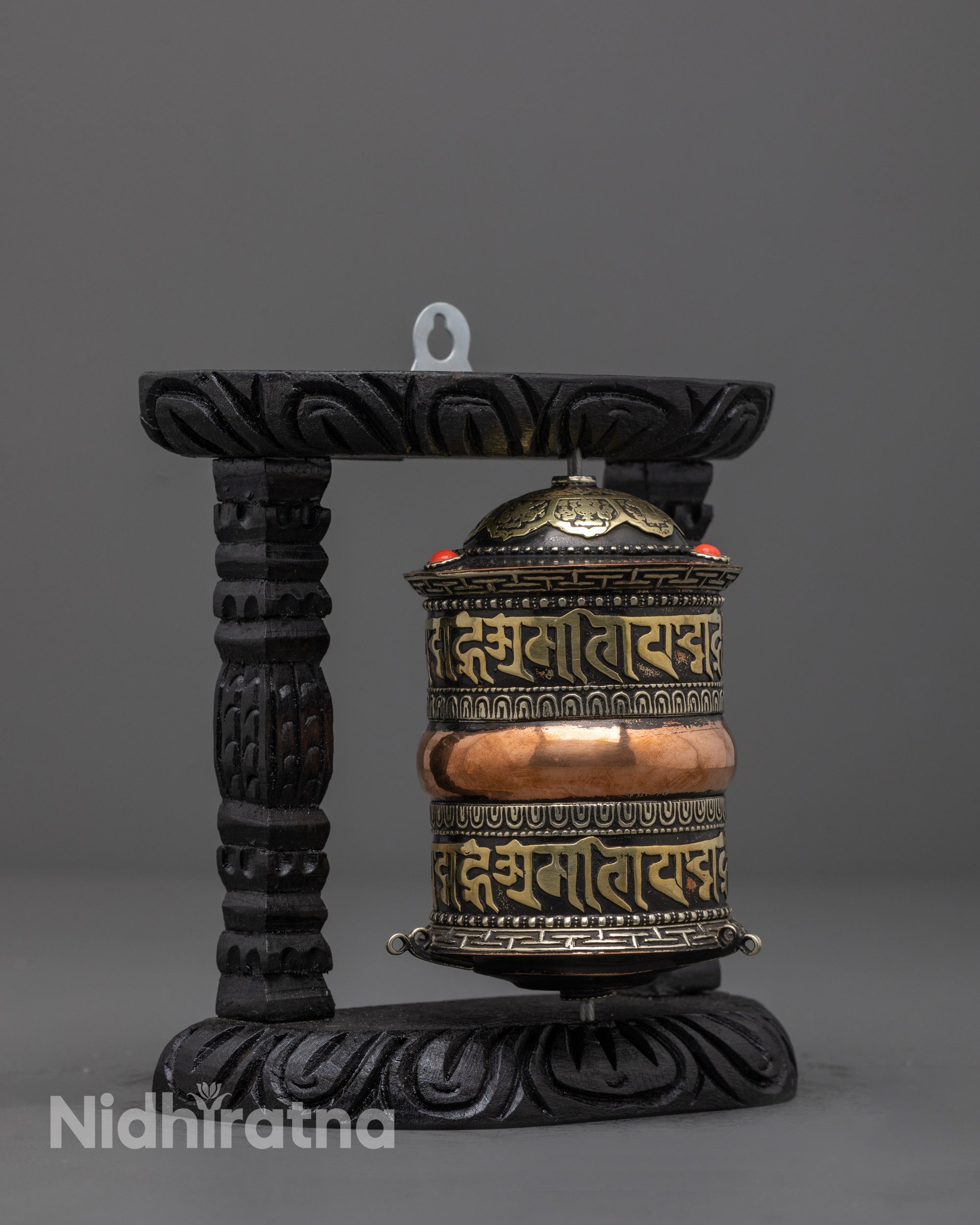 Side angle of handcrafted copper Buddhist prayer wheel on dark wood frame
