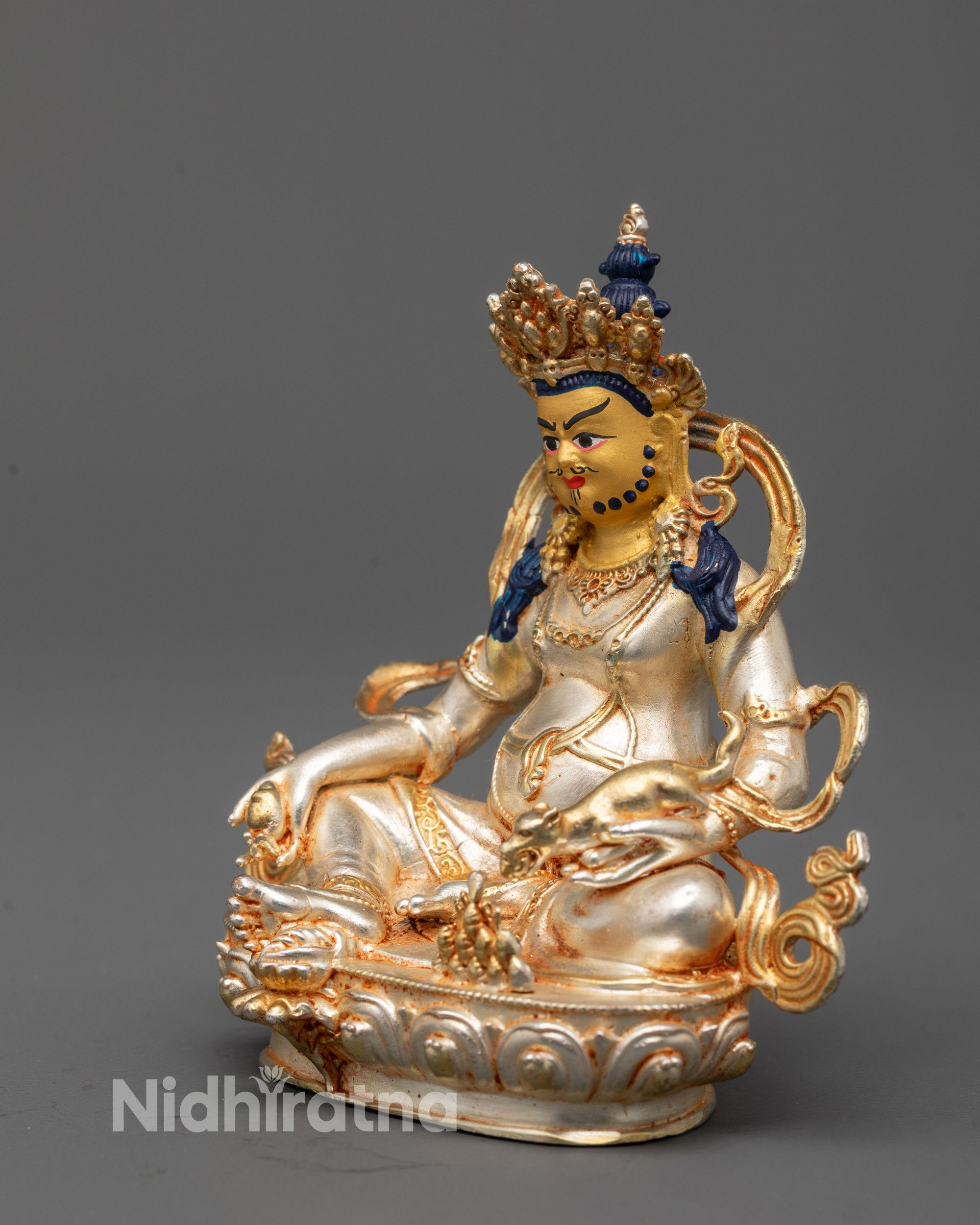 Side angle of silver-plated Dzambhala idol holding citron fruit and mongoose