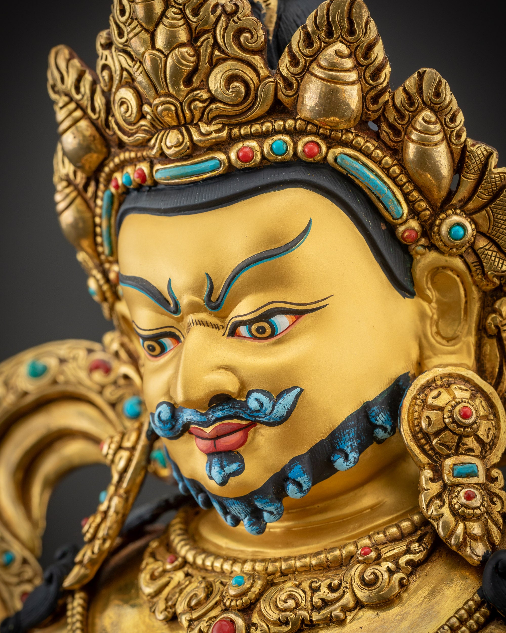 Side close up face of Dzambhala statue showing crown, earrings, and detailed facial features

