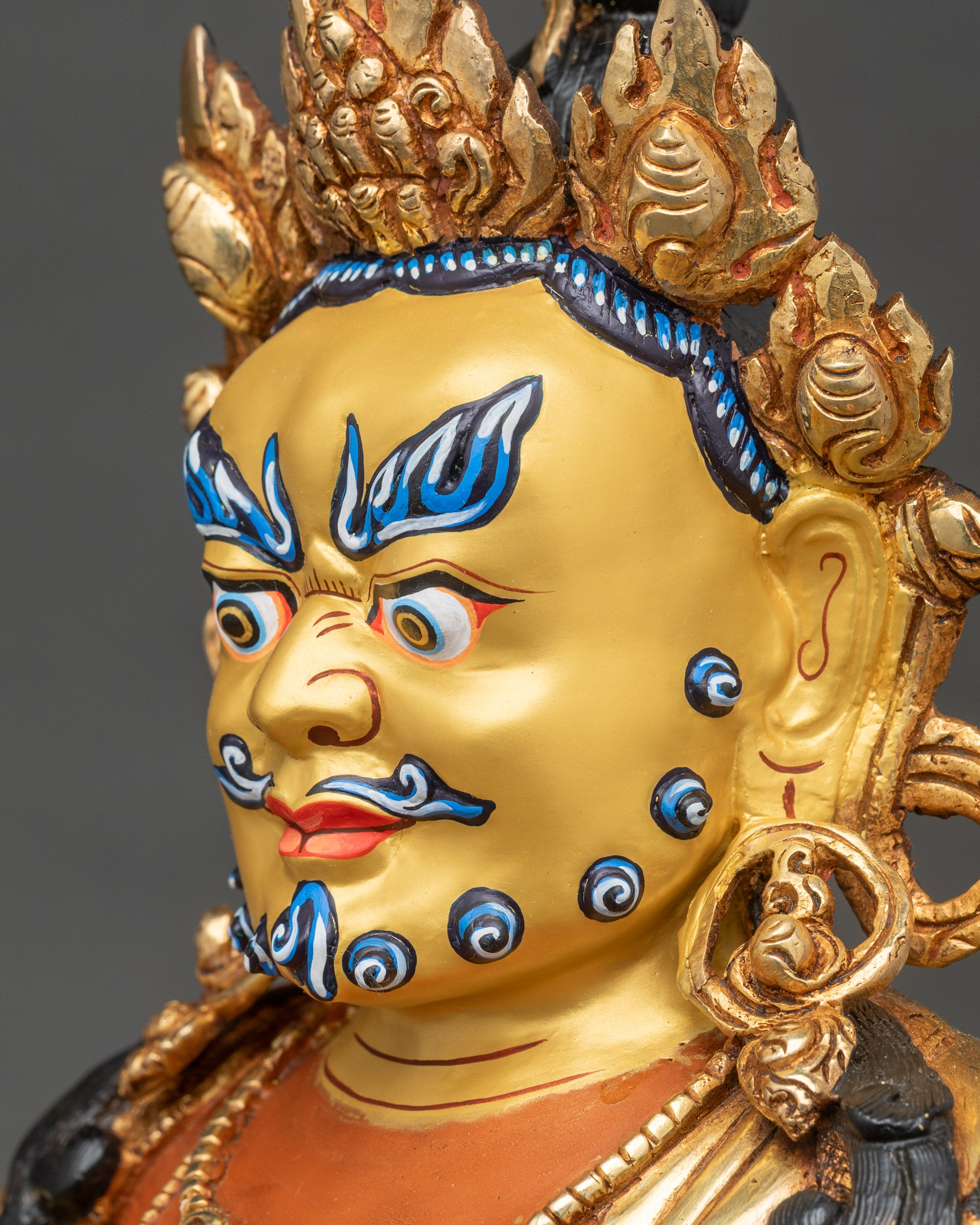 Side face close-up of Dzambhala deity with gilded crown and earrings