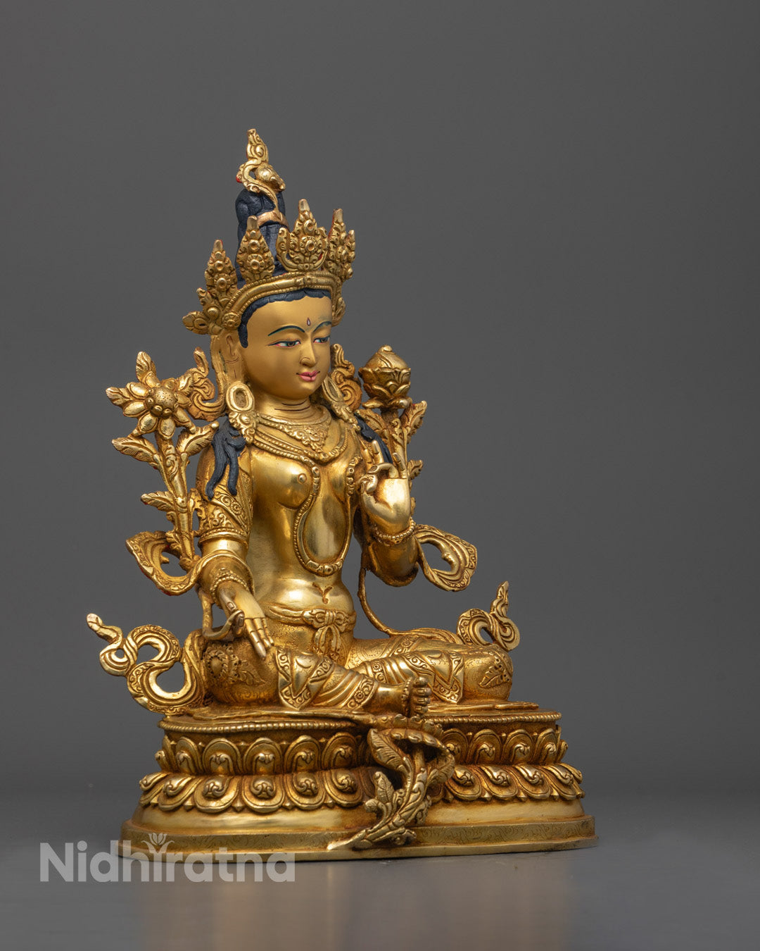 Side view of Green Tara statue seated in royal ease on a layered lotus base
