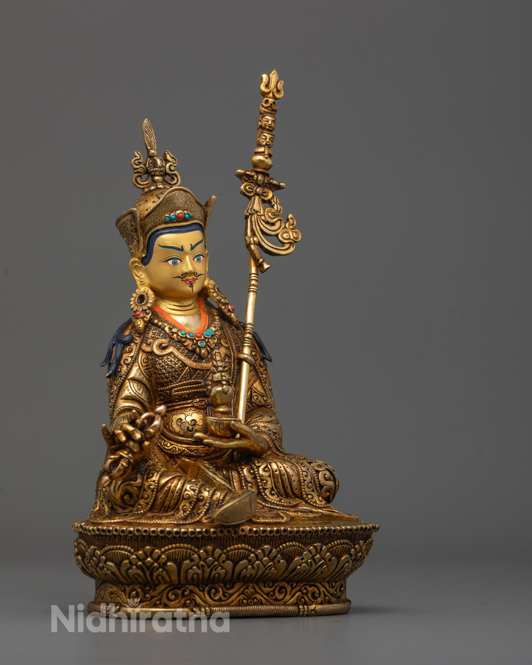 Side view of Guru Rinpoche statue highlighting khatvanga trident and intricate robe carvings
