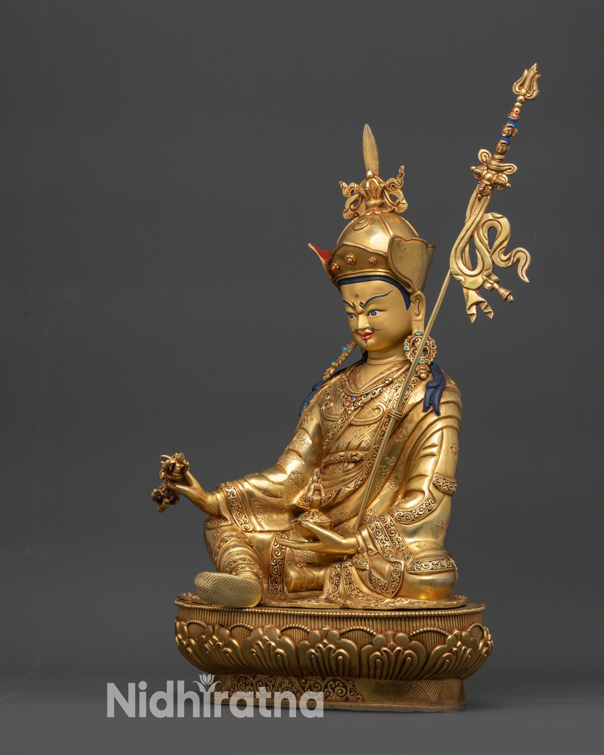 Side view of Guru Rinpoche statue on lotus base with layered robe textures
