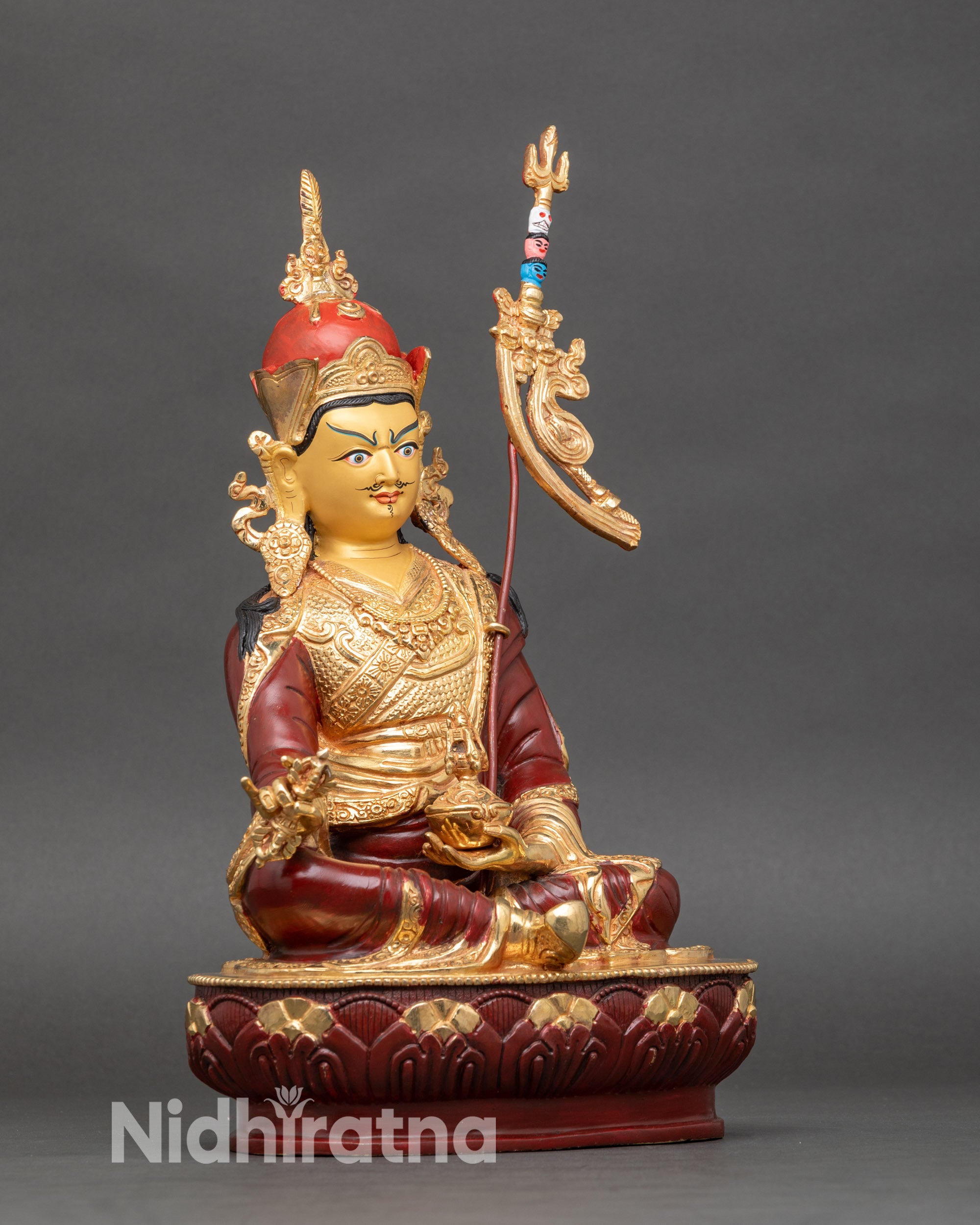 Side view of Guru Rinpoche statue with lotus hat, kasaya robe, and trident resting on shoulder