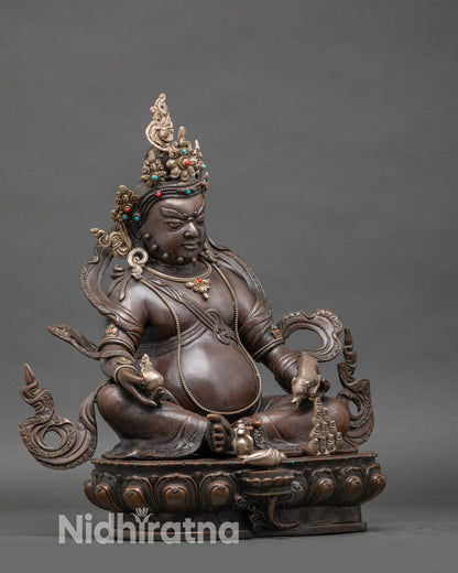 Side view of Himalayan Dzambhala sculpture with mongoose releasing blessings, silver-plated Buddhist deity