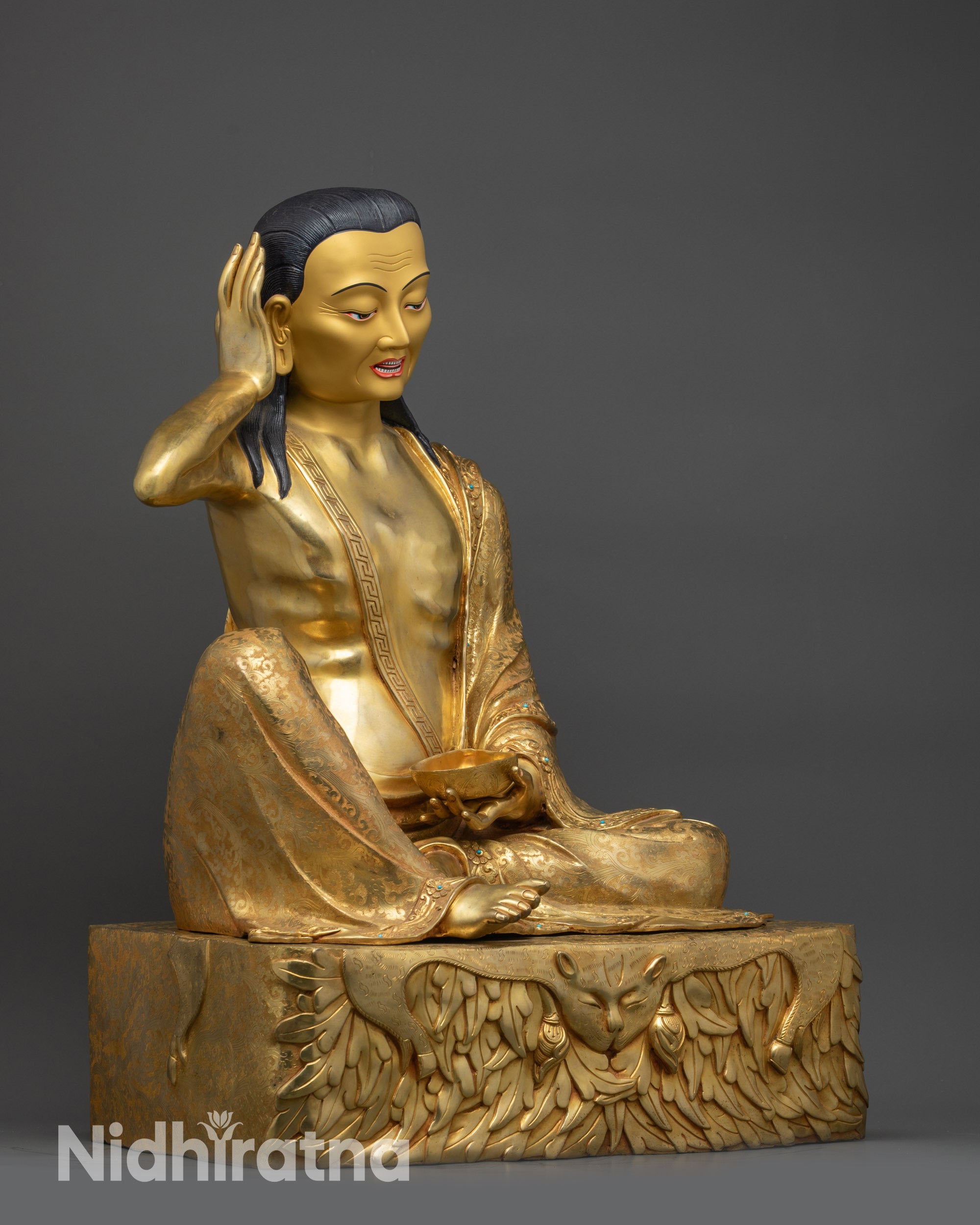 Side view of Milarepa seated on deer skin-draped pedestal holding kapala ritual cup
