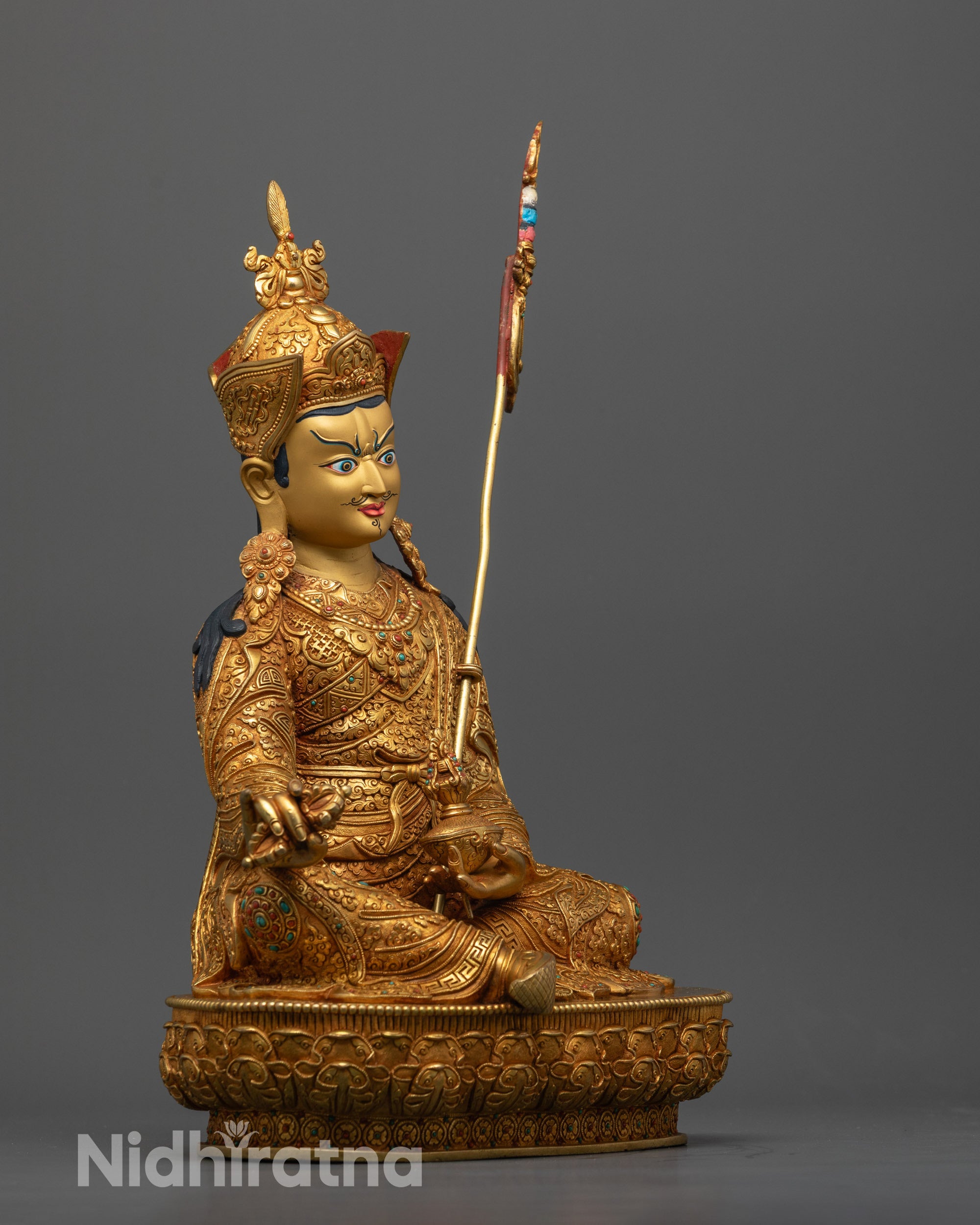 Side view of Padmasambhava statue holding khatvanga trident and vajra in lotus seat