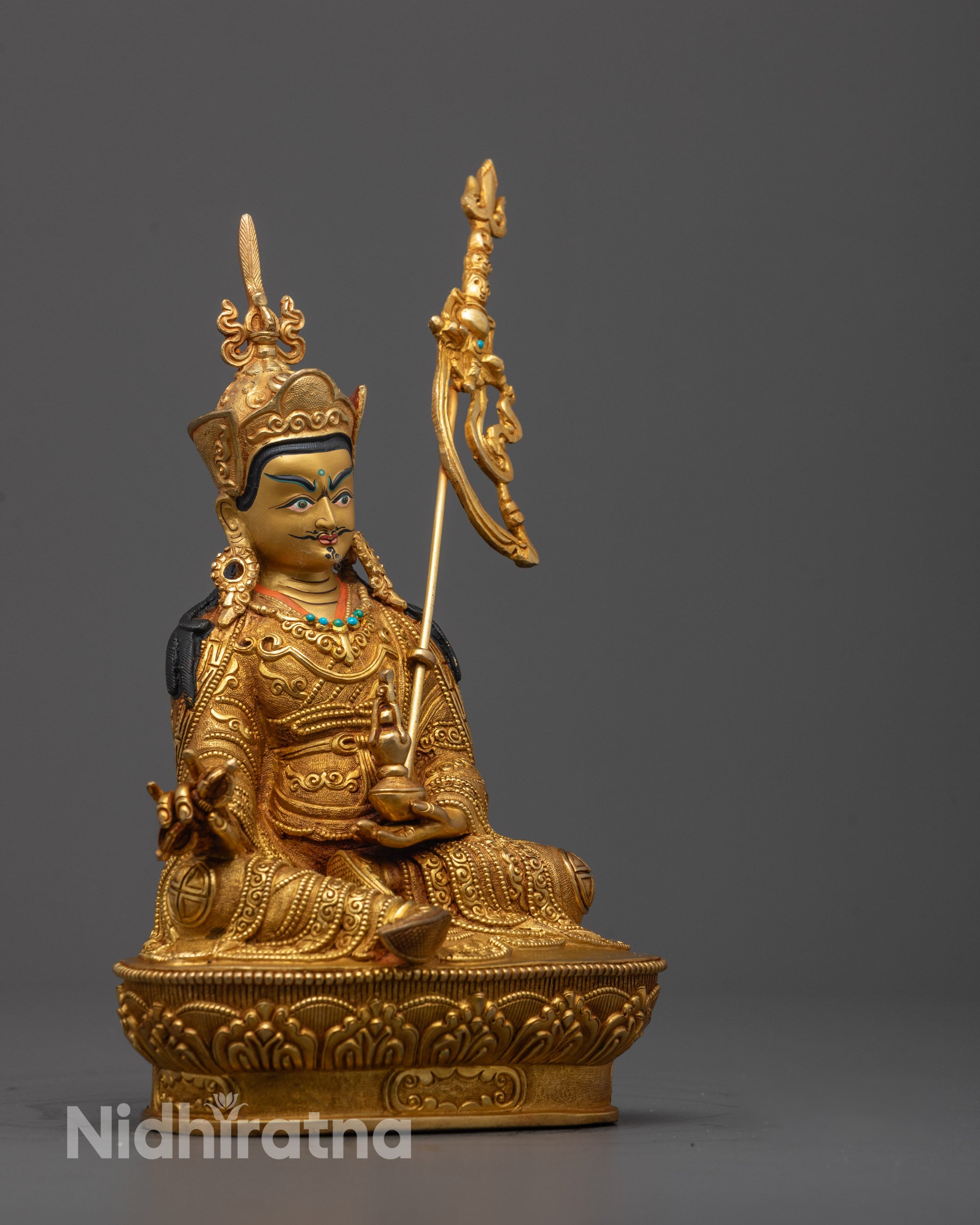 Side view of Padmasambhava statue holding skull cup and vase with intricate gold details